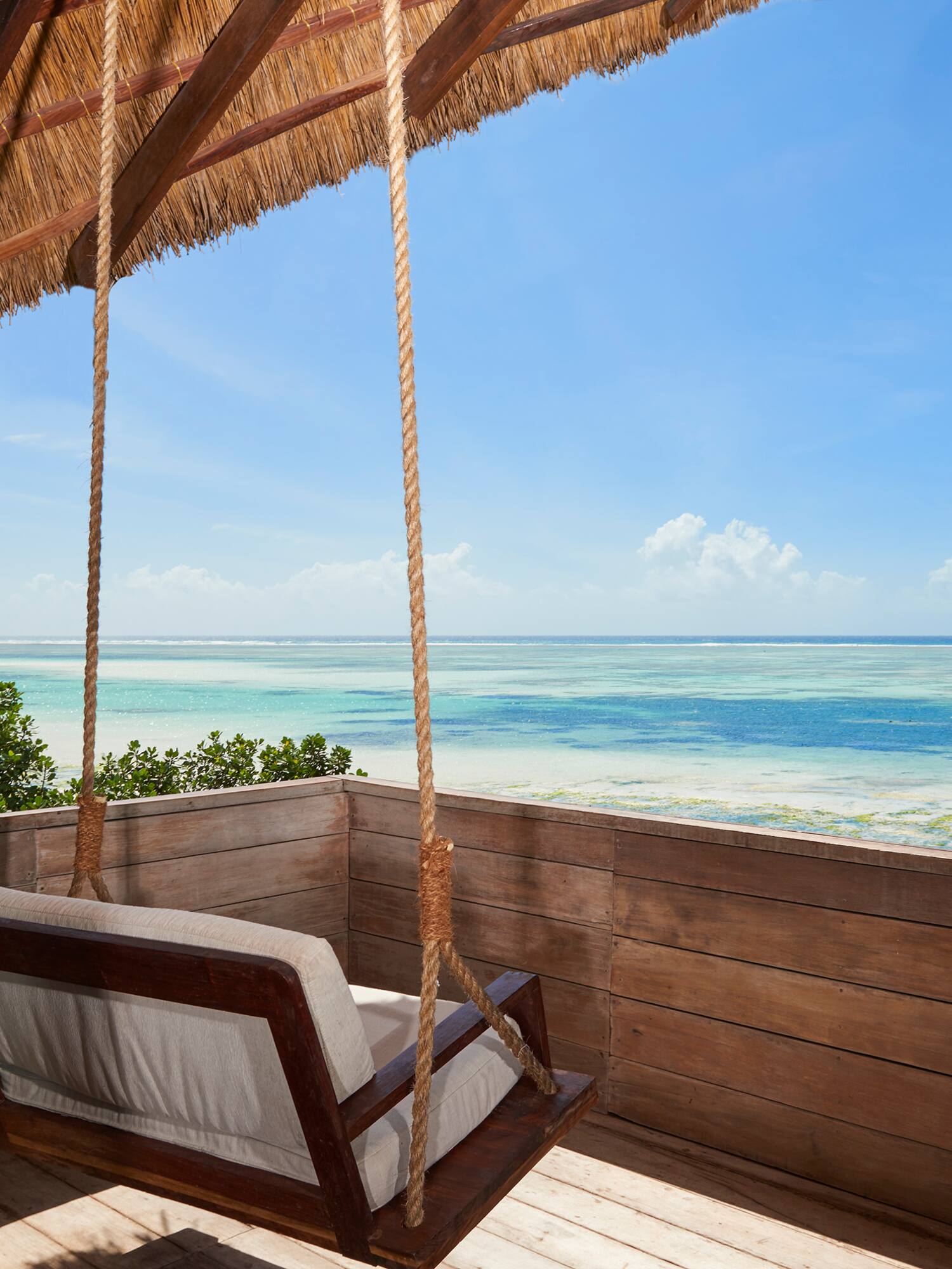Tropical ocean view from a thatched balcony with a wooden swing.