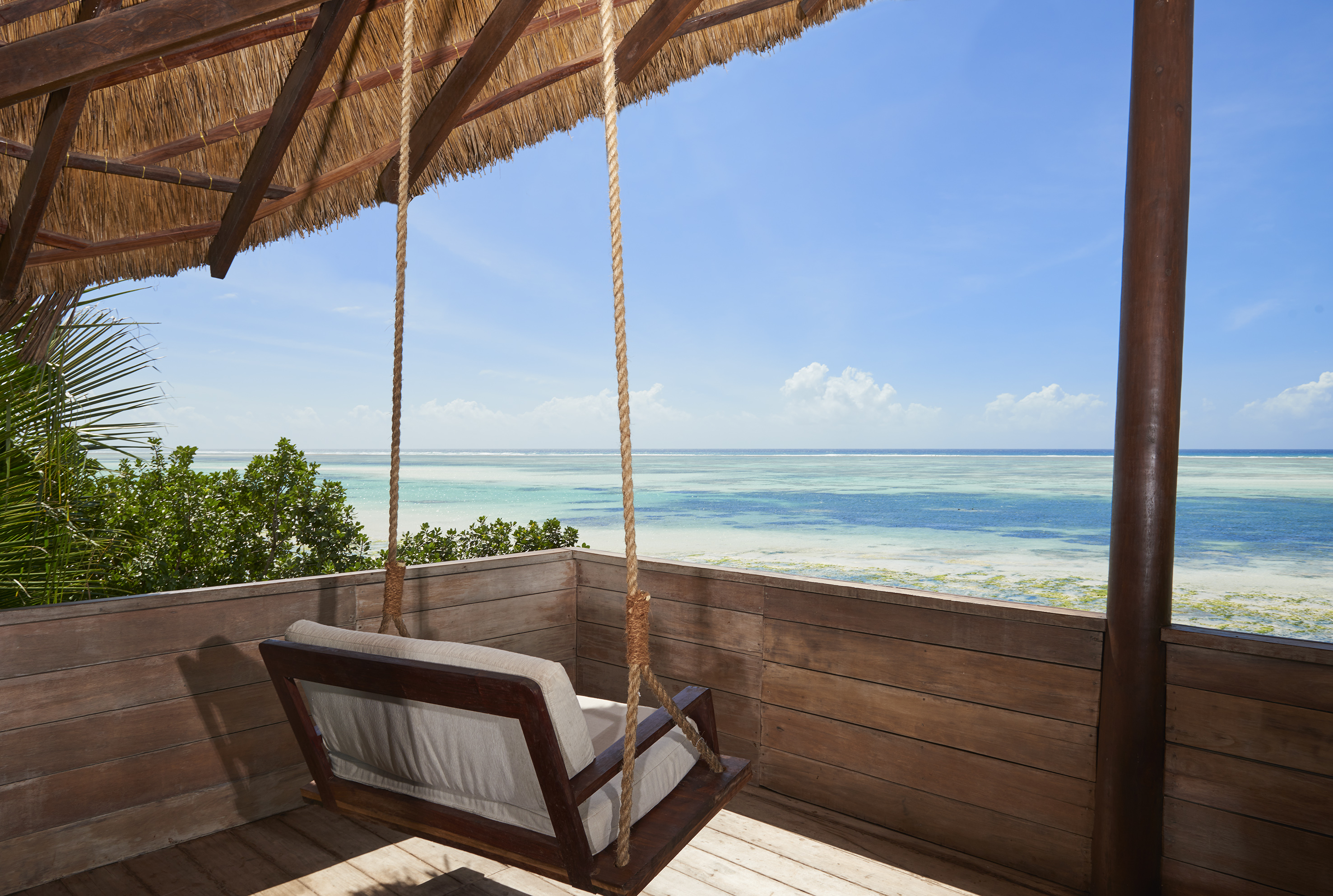 Tropical ocean view from a thatched balcony with a wooden swing.