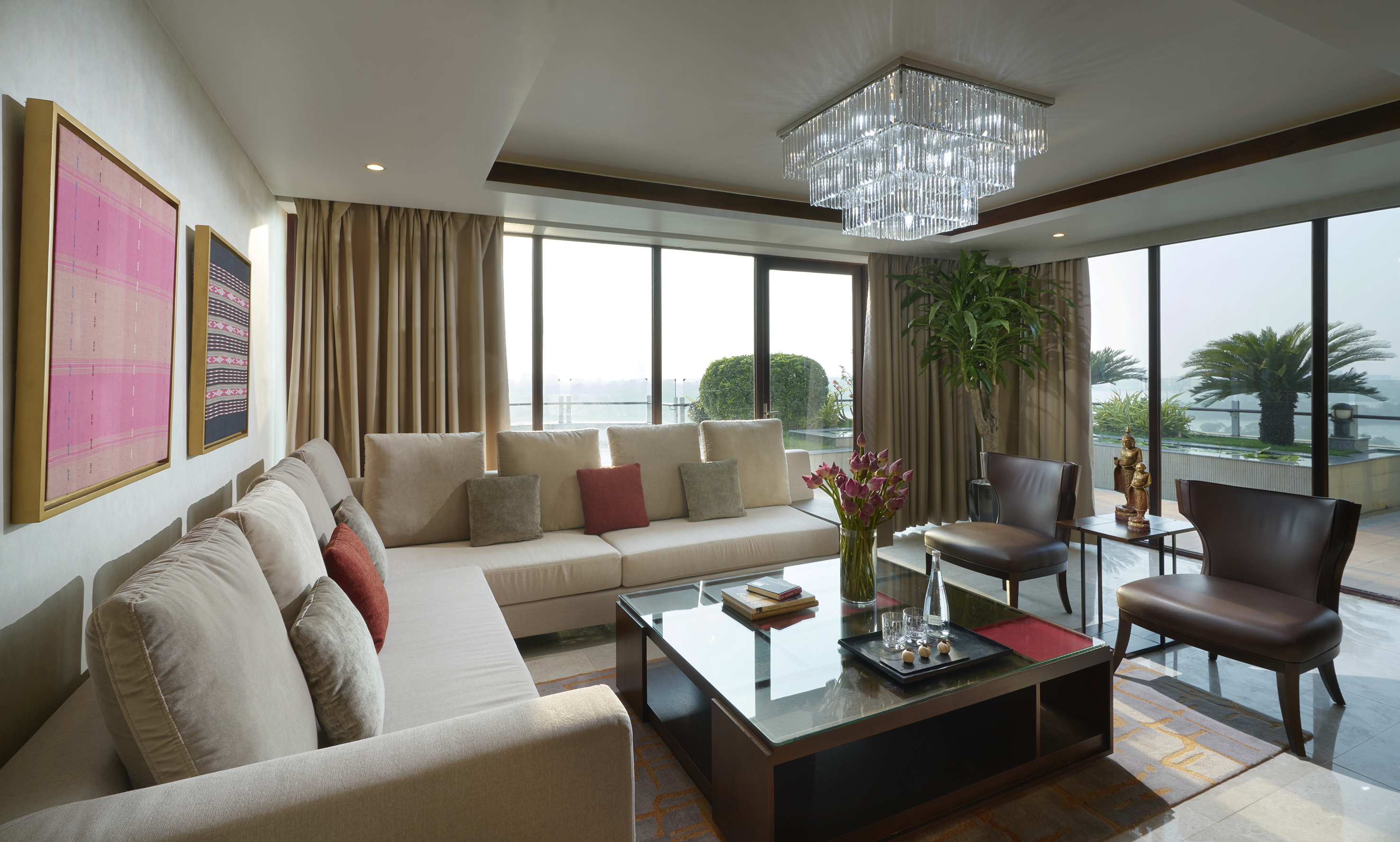 Modern living room with sofa, glass table, chandelier, and panoramic windows.