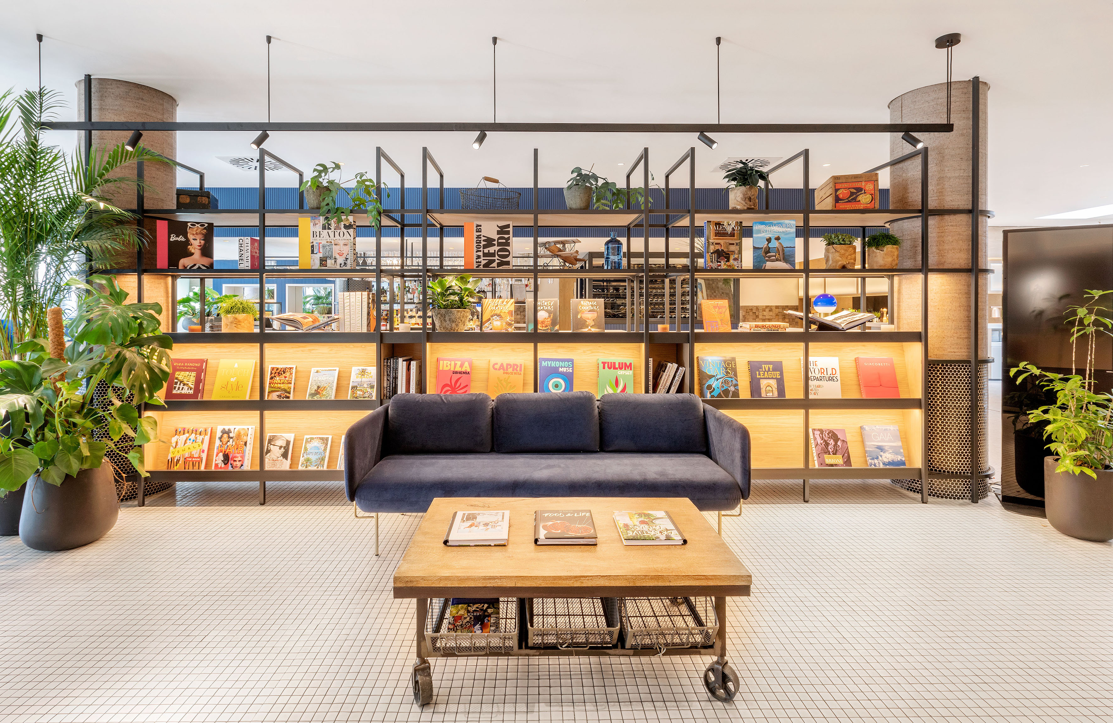 Modern hotel lounge with illuminated bookshelf, stylish books, blue sofa, wood table.