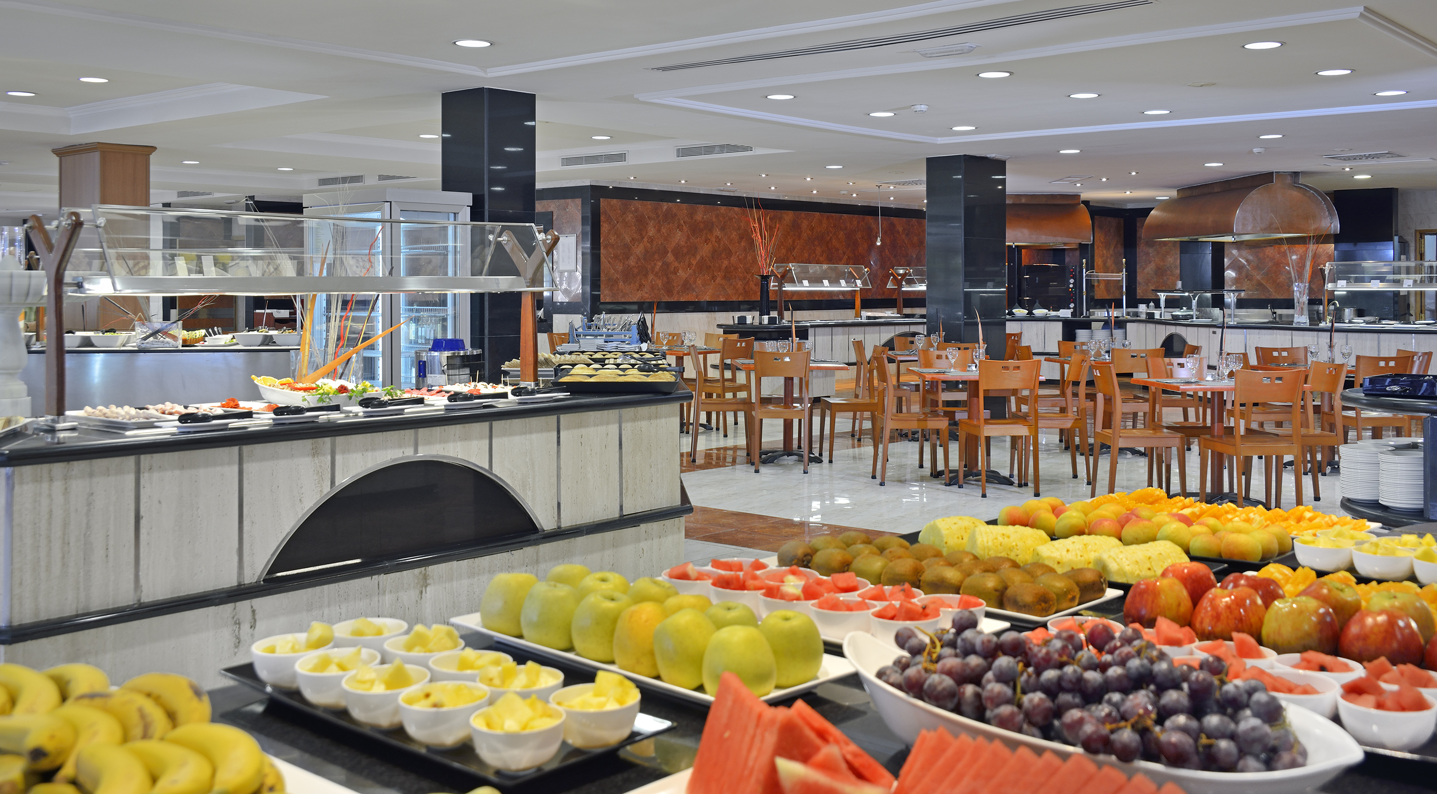 Hotel buffet with vibrant fresh fruit, salad bar, and modern dining room.