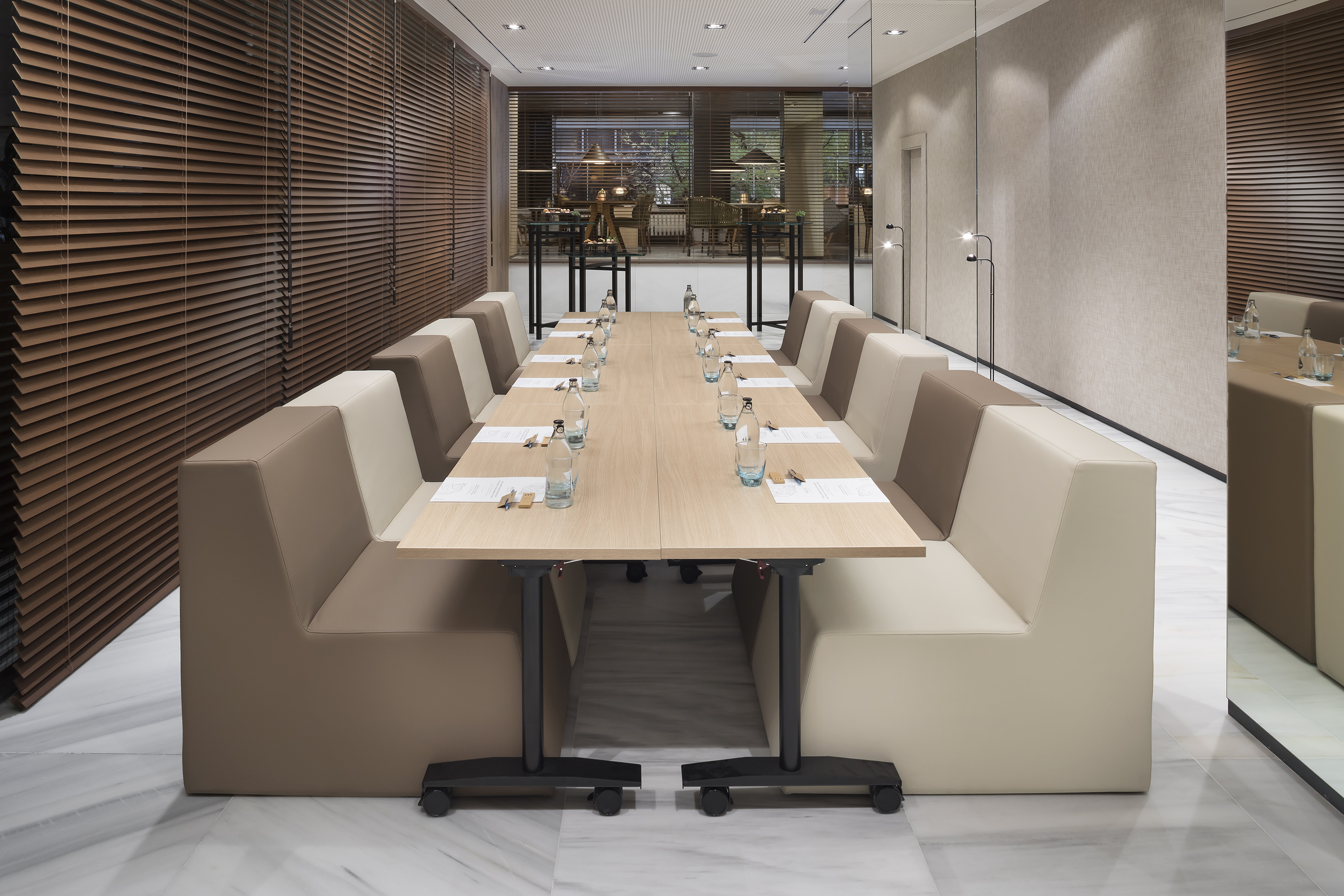 Modern meeting room with long table, two-tone banquette seating, wood blinds.