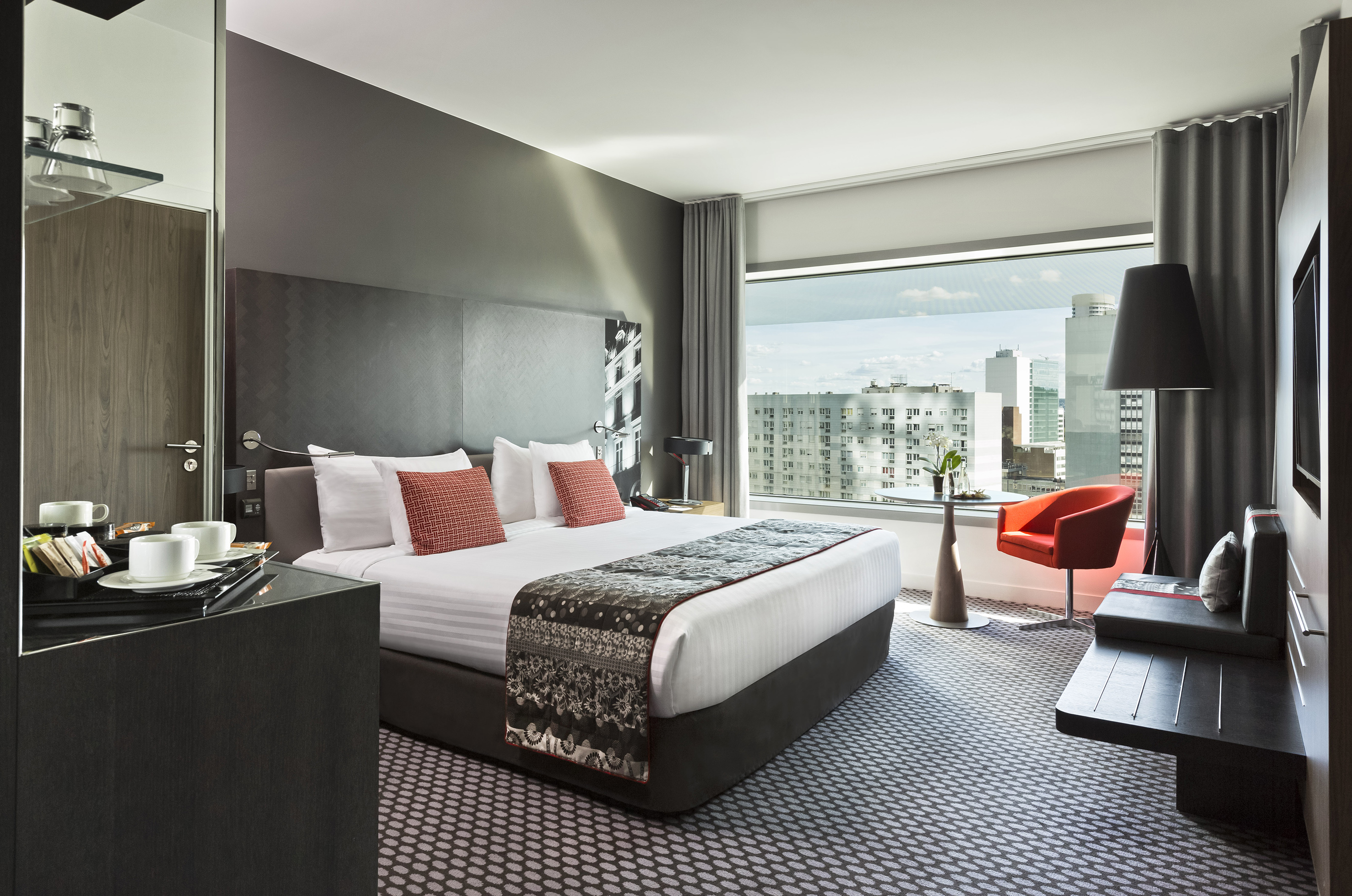Luxury hotel room with king bed, panoramic city view, and modern furnishings.