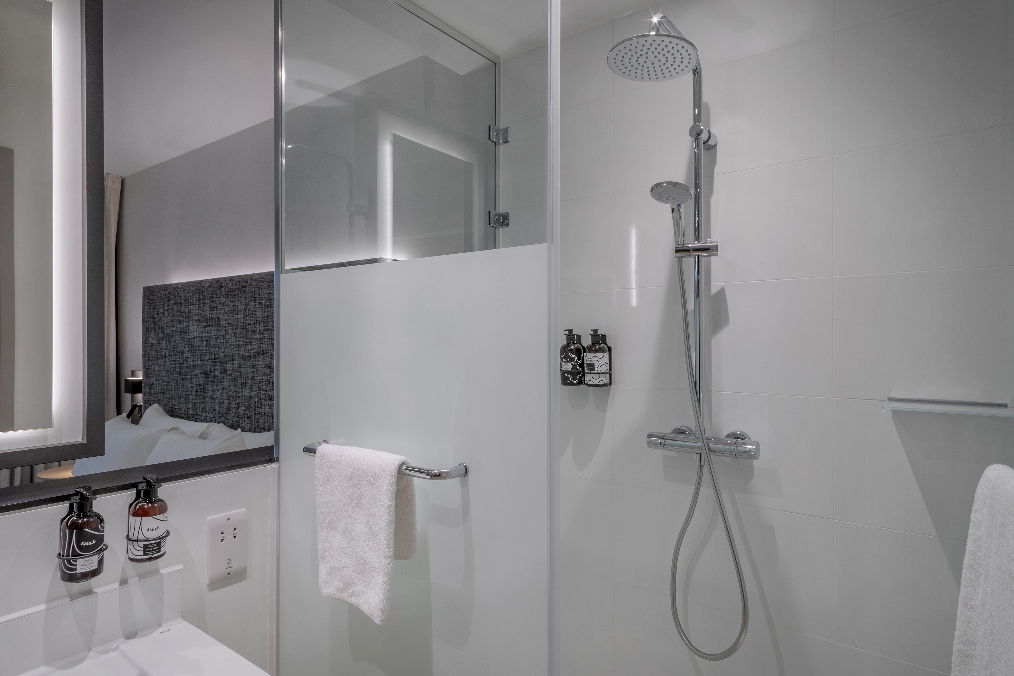 Modern shower with glass enclosure, rain head, white tiles, and hotel toiletries.