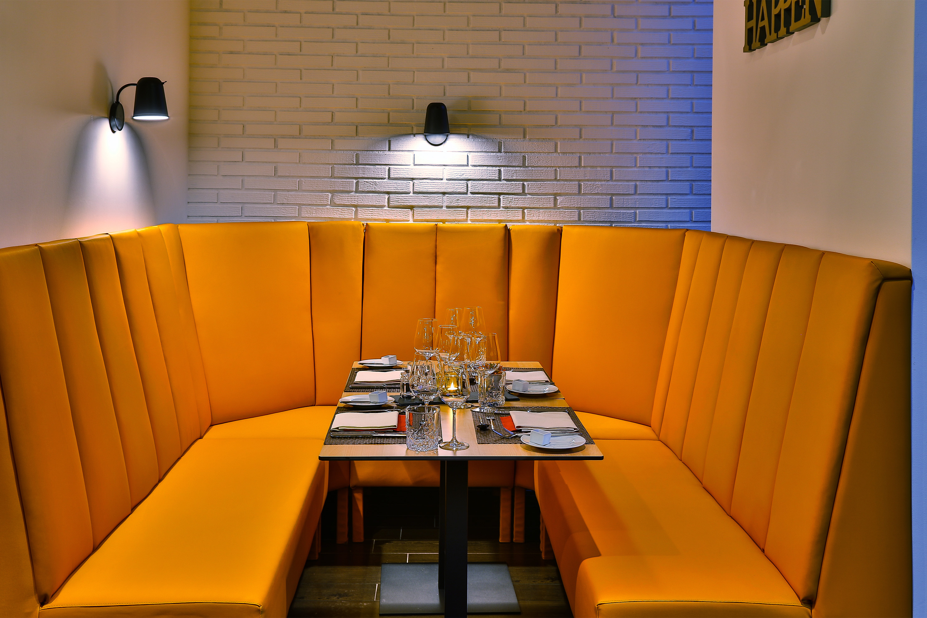 Orange restaurant booth seating and set dining table against brick wall.