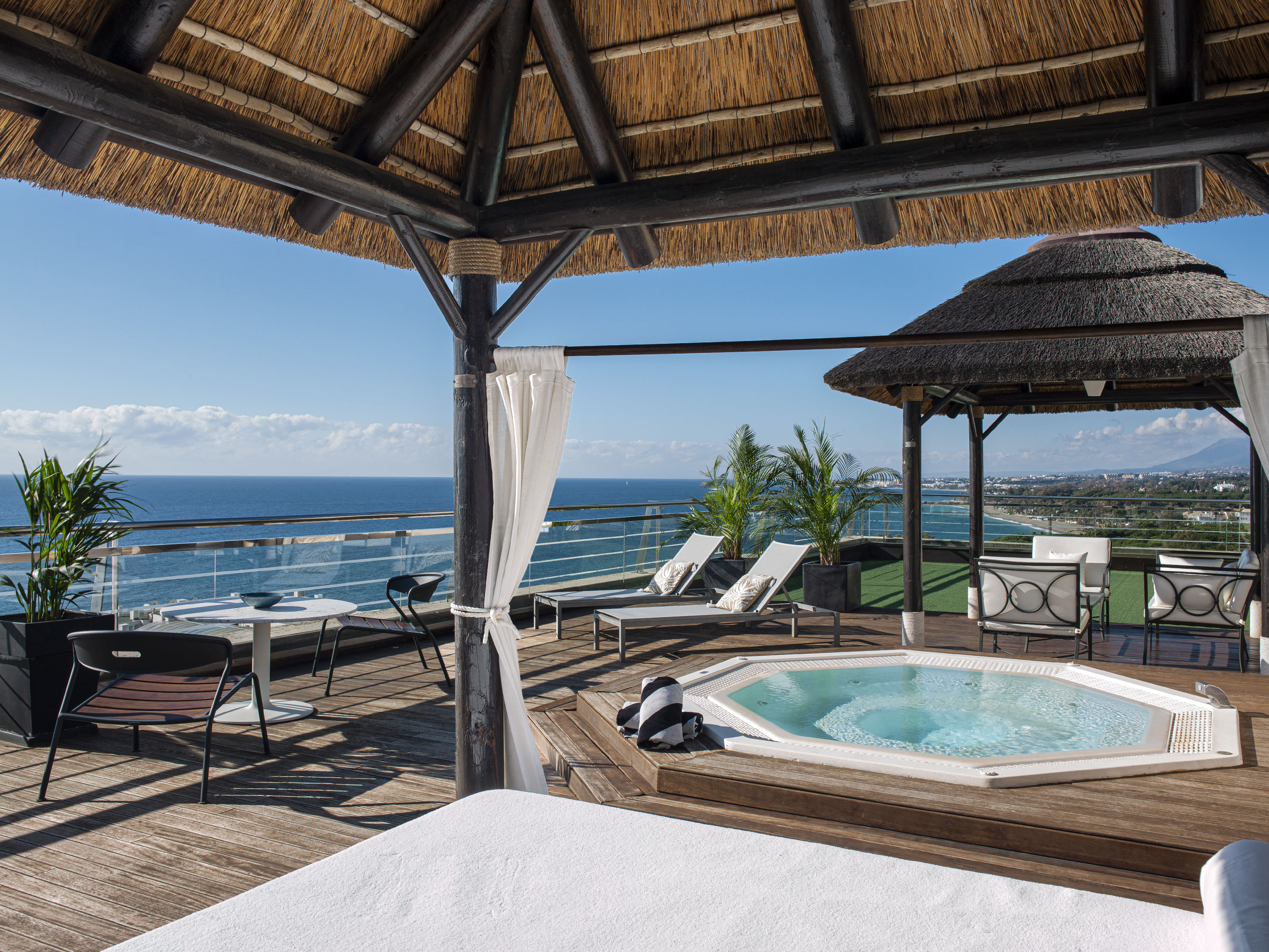 Rooftop terrace with ocean view, hot tub, thatched roof, and sun loungers.