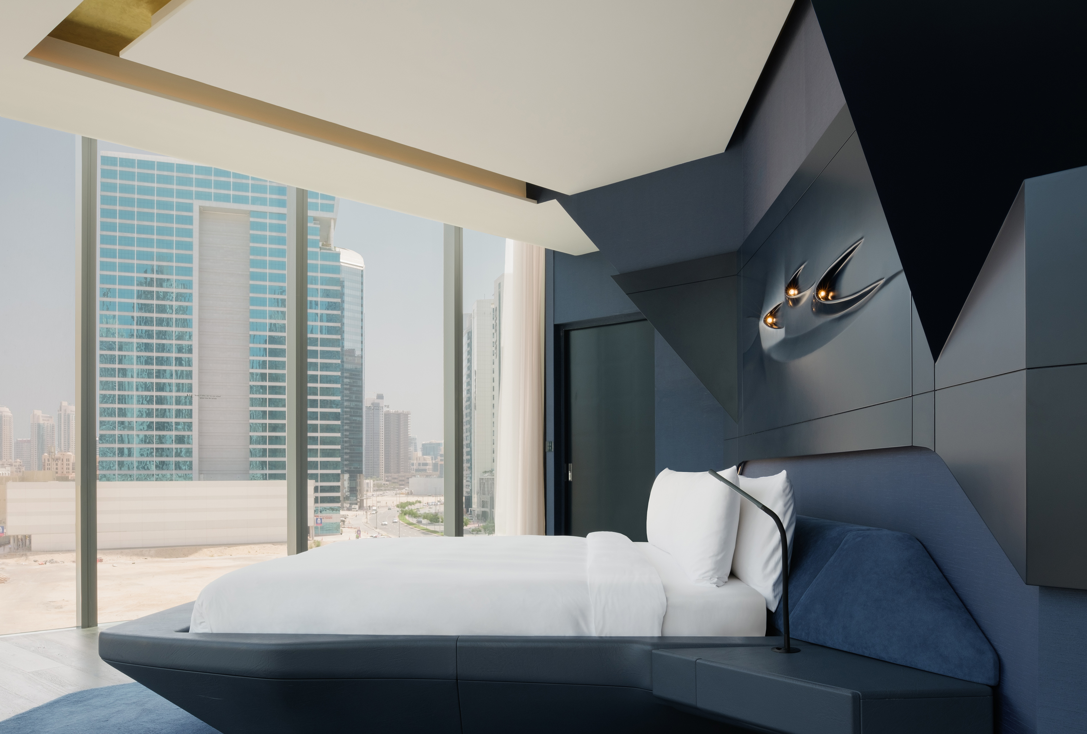 Luxury modern bedroom with city view, dark blue bed, and geometric wall decor.