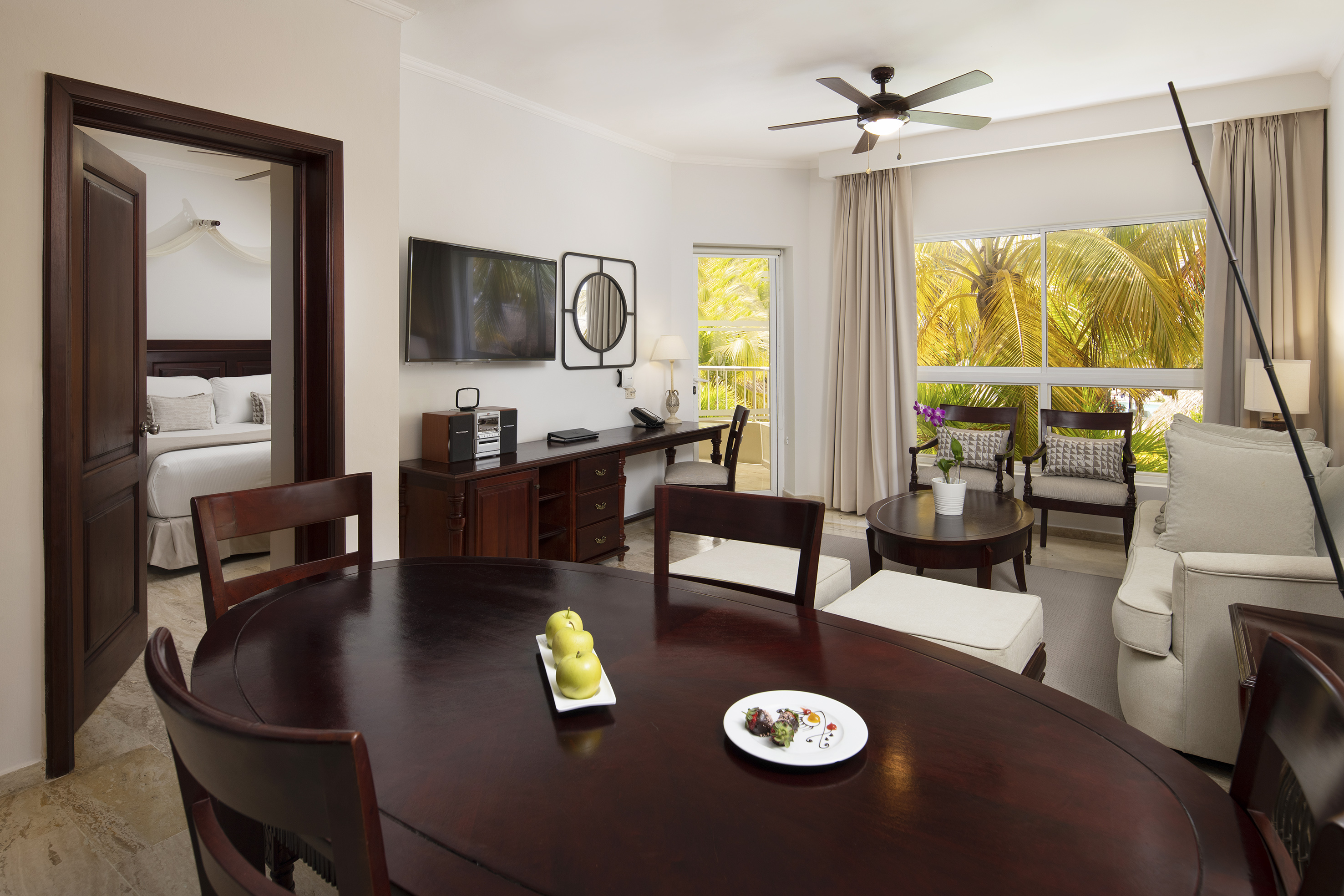 Spacious hotel suite: dining table, living room, and vibrant tropical view.
