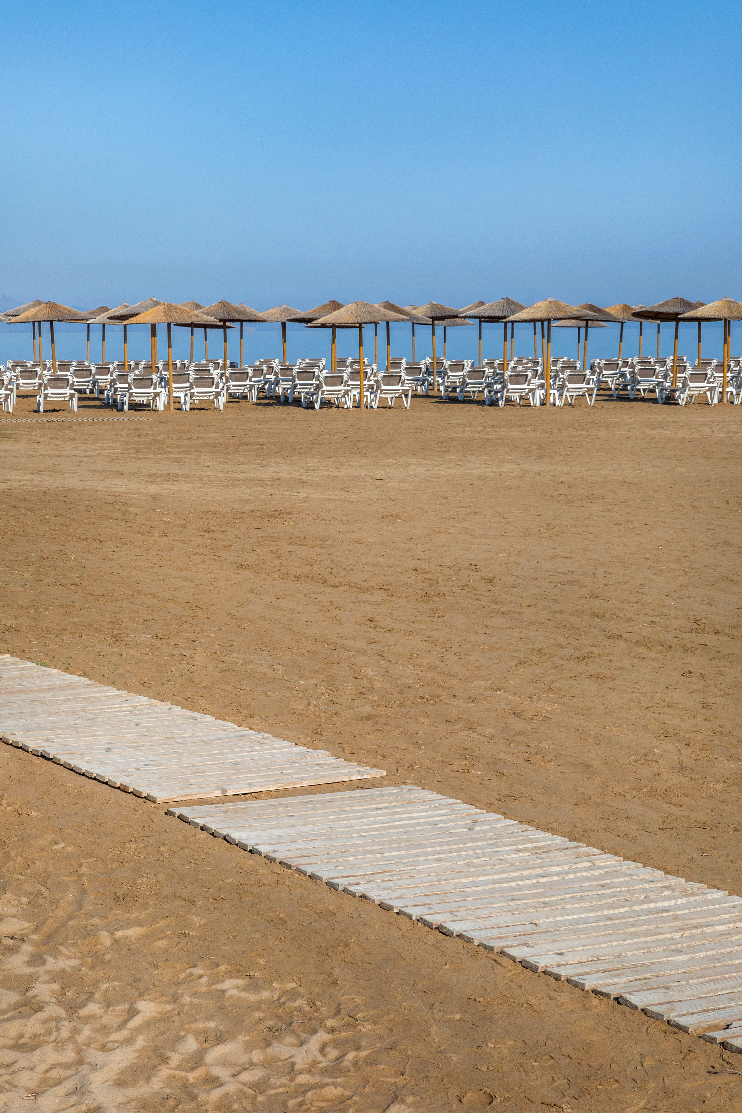 Beach with boardwalk, straw umbrellas, lounge chairs, and calm blue sea.