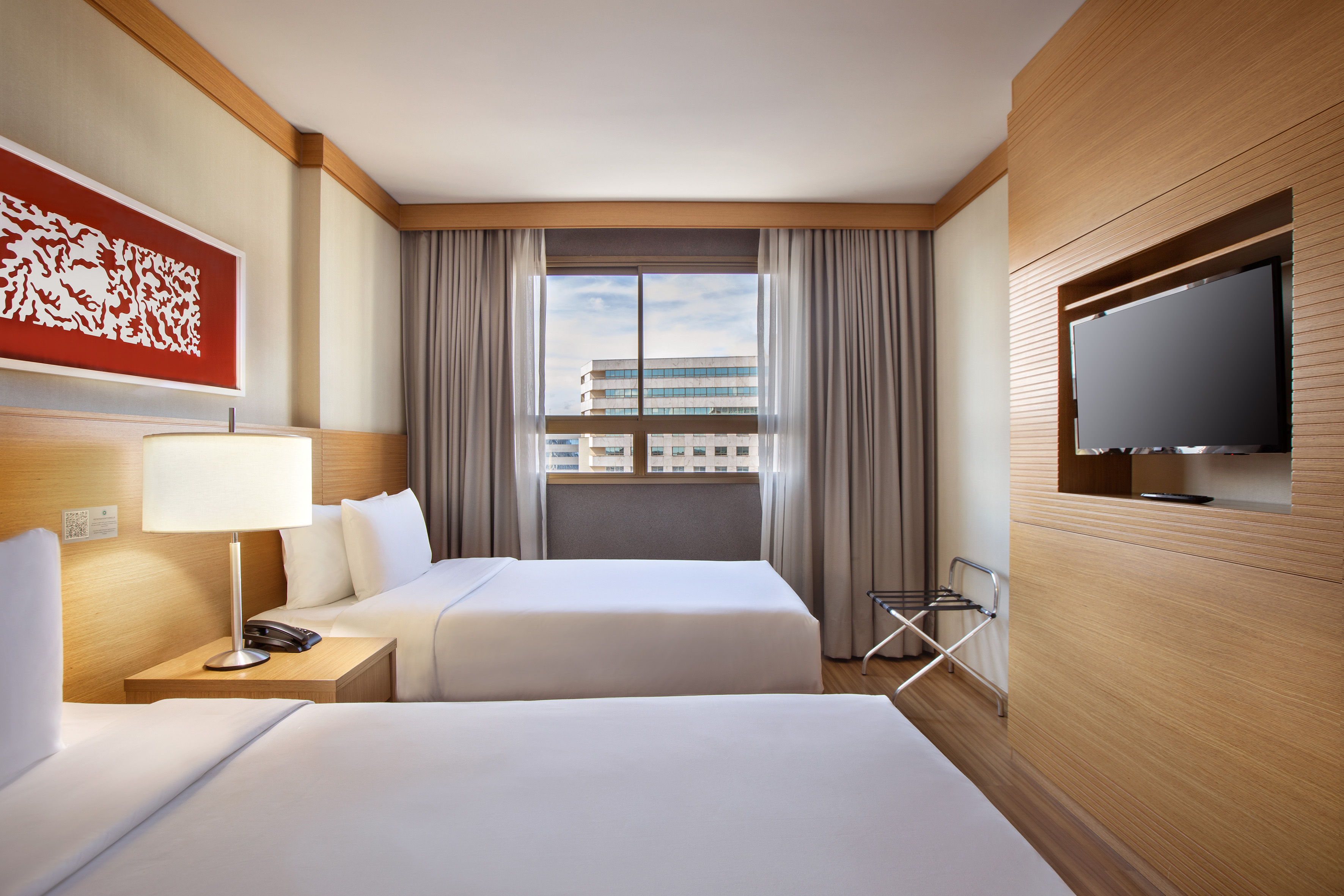 Modern hotel guest room with two twin beds, window, and wall-mounted TV.