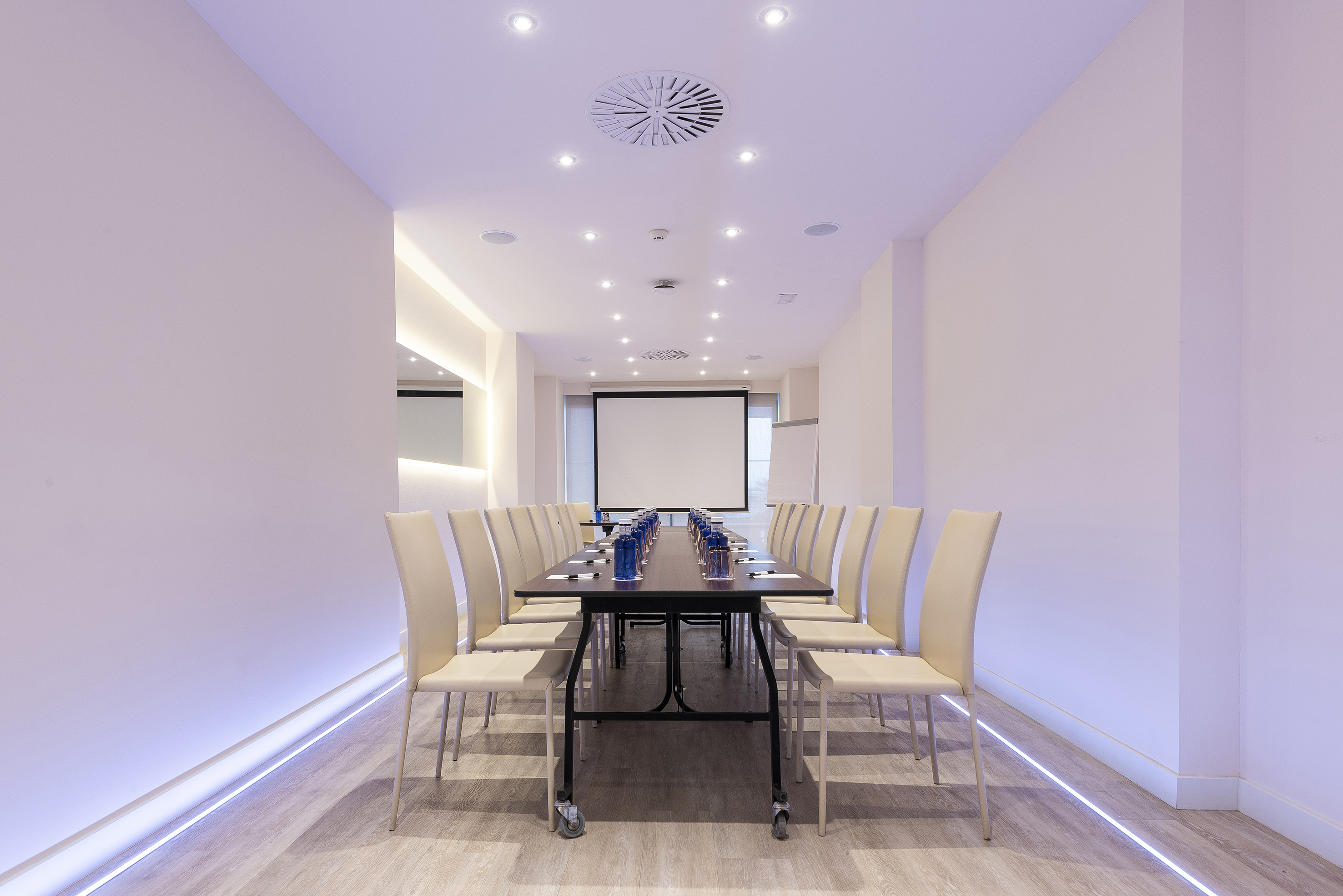 Modern conference room with long table, beige chairs, and projection screen.