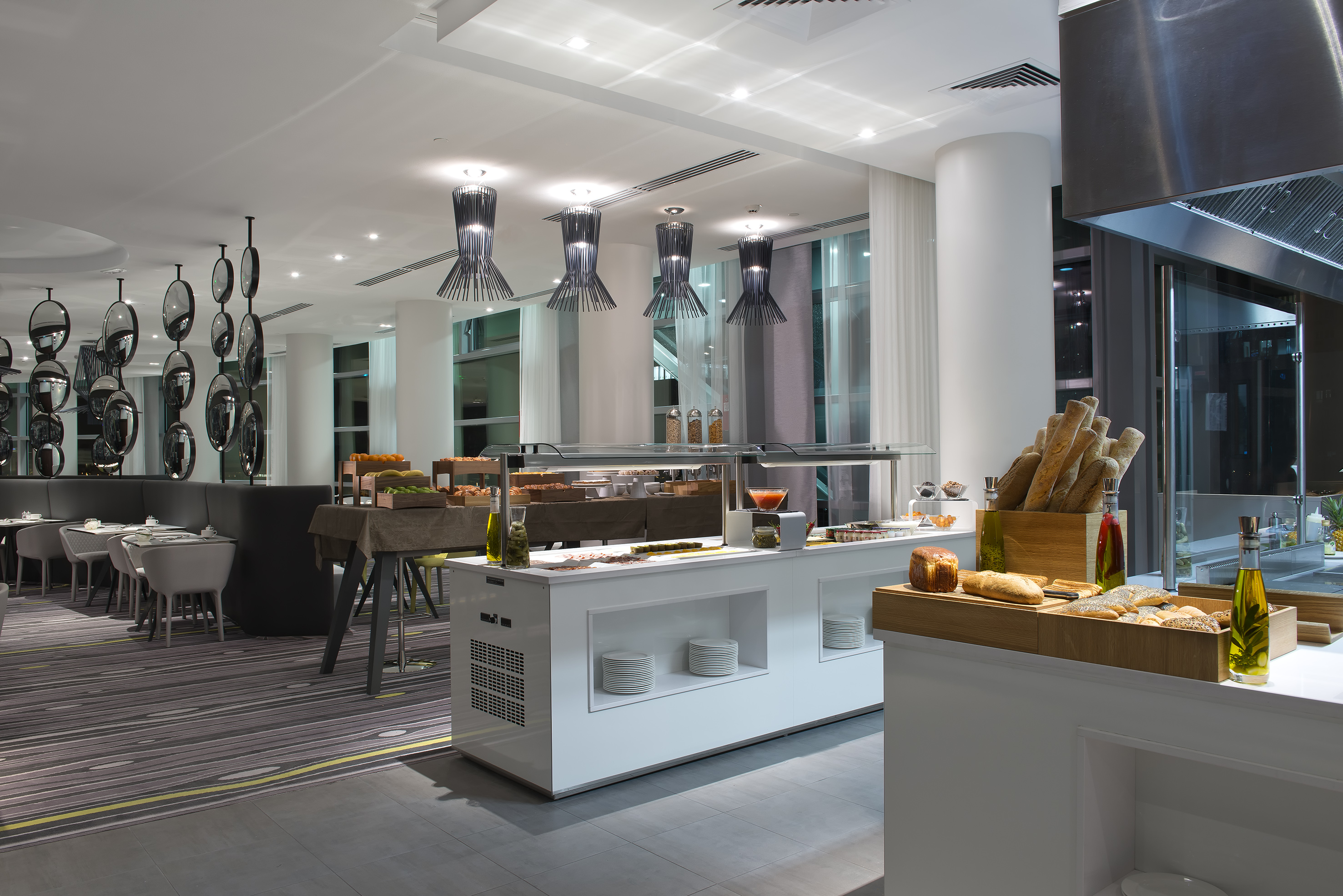 Modern hotel restaurant buffet with breakfast food, elegant lighting, and seating.