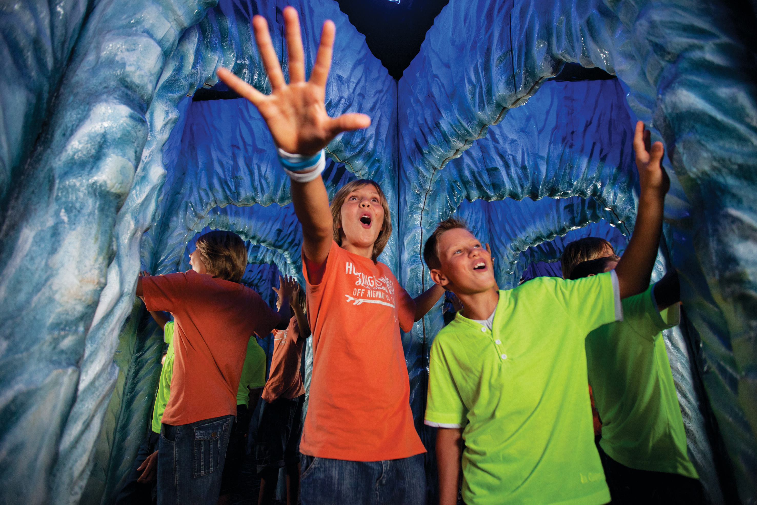 Kids reacting with wonder in a vibrant blue cave or tunnel attraction.