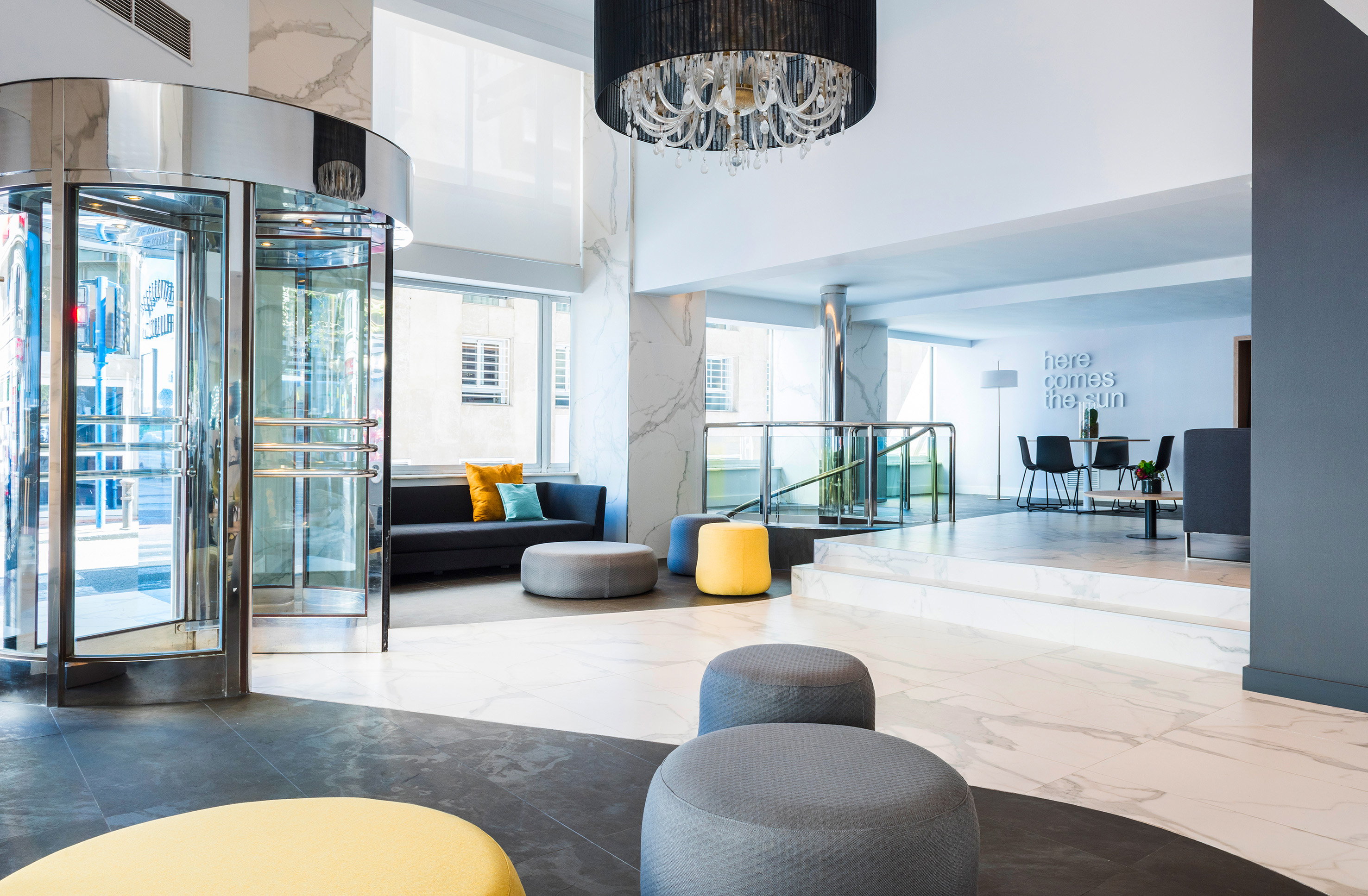 Modern hotel lobby with revolving door, marble walls, and colorful ottomans.