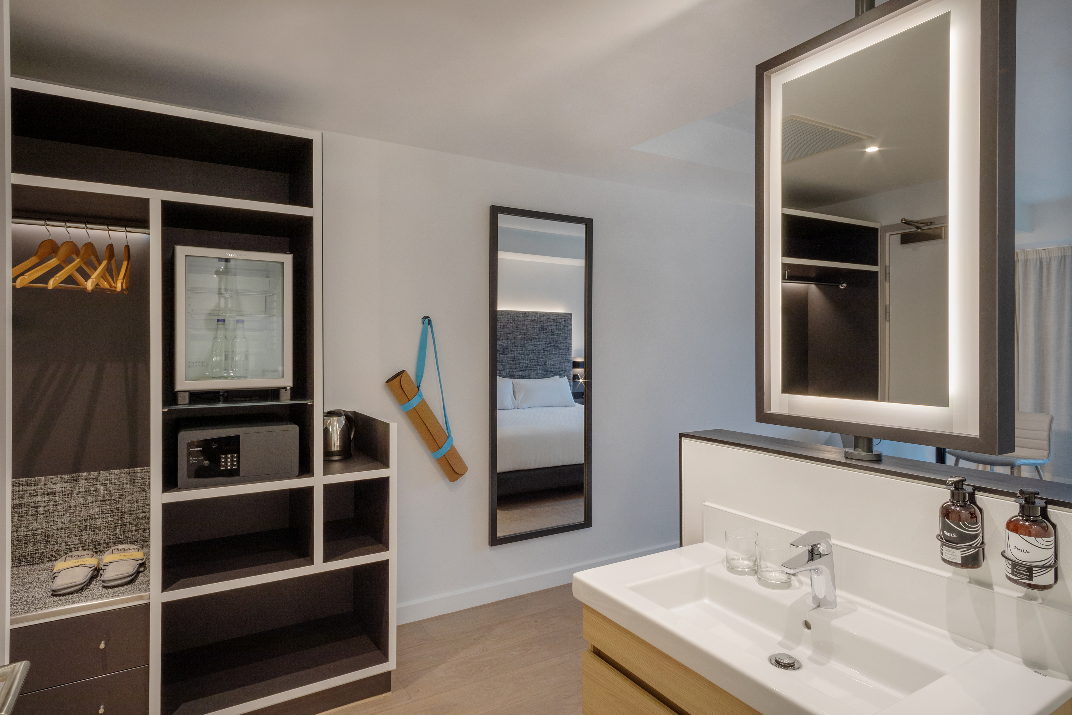 Hotel room with wardrobe, minibar, safe, vanity, lit mirror, and yoga mat.