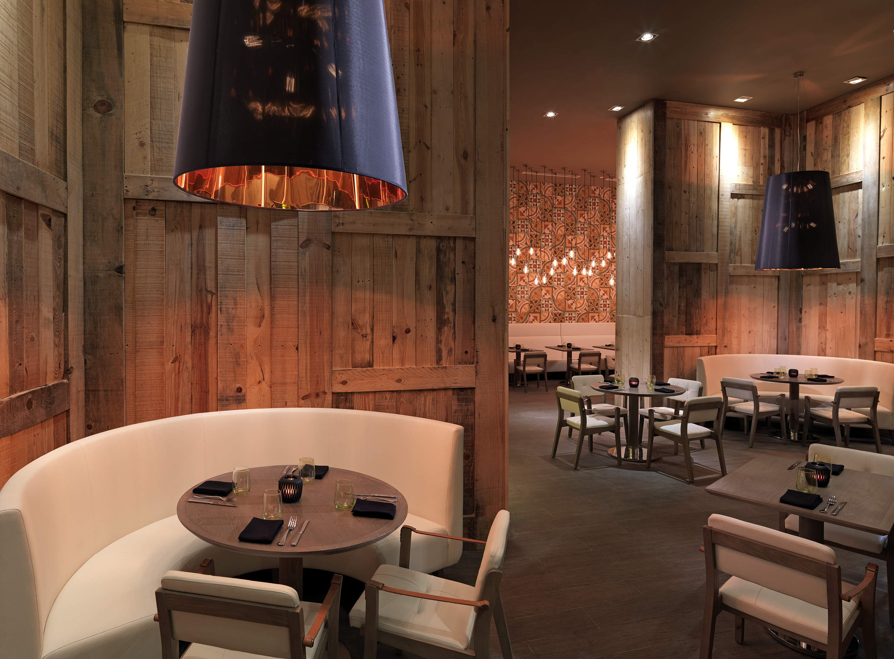 Modern restaurant with wooden walls, white booths, and pendant lights.