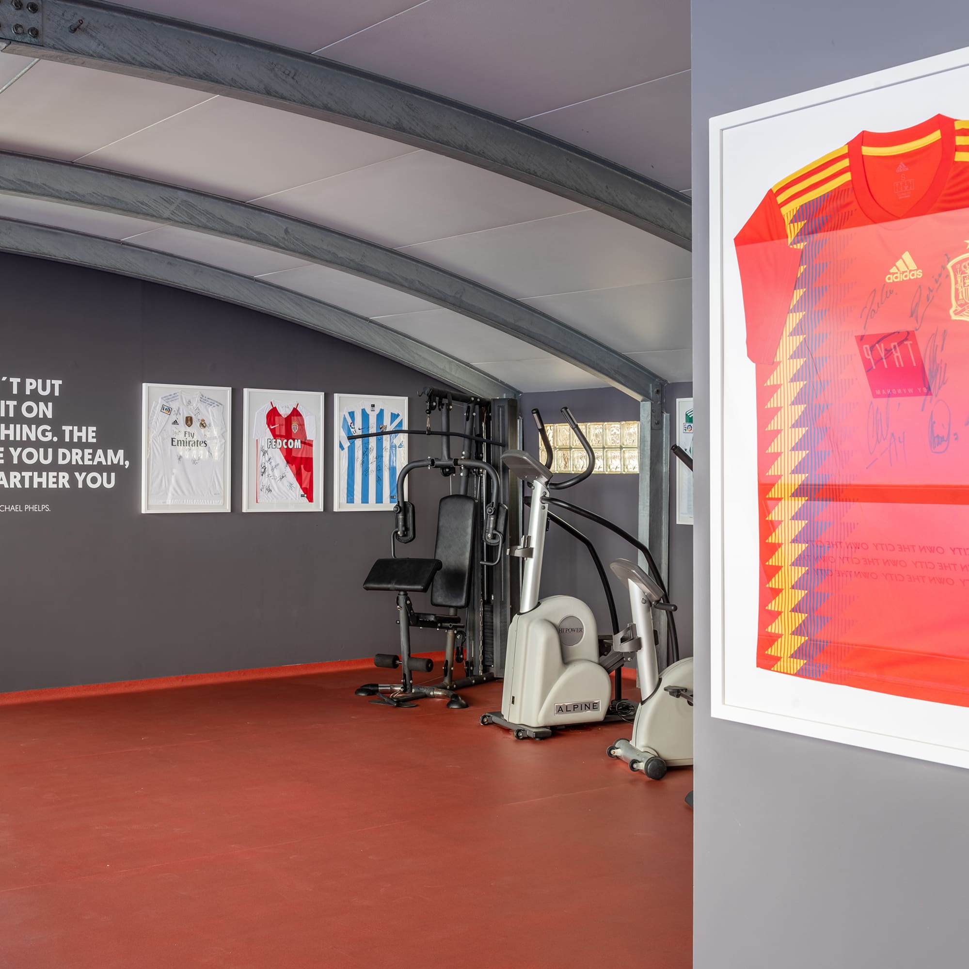 Home gym with signed sports jerseys, workout equipment, and motivational quote.