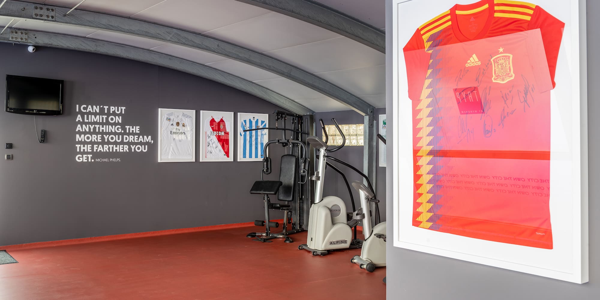Home gym with signed sports jerseys, workout equipment, and motivational quote.