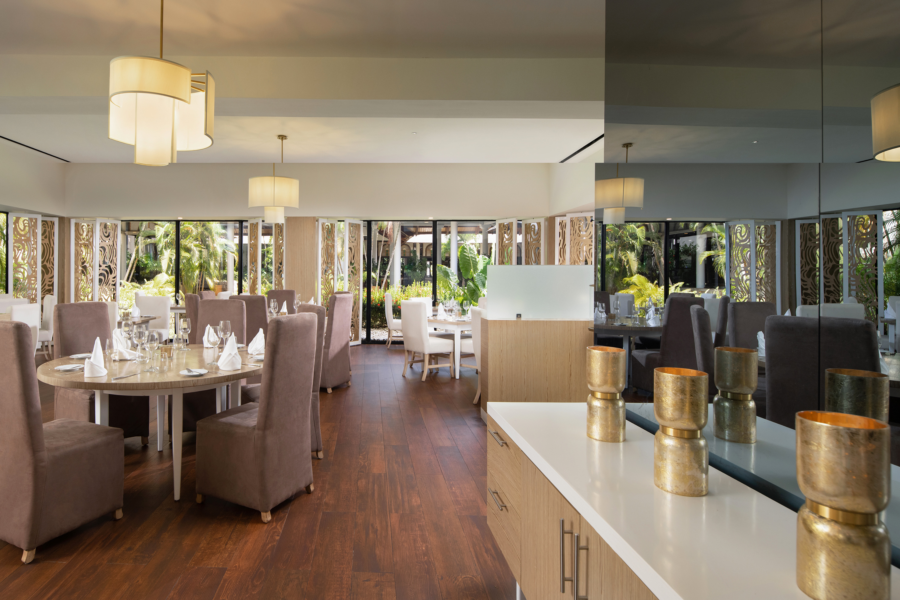 Modern upscale restaurant with set tables, wood floor, and tropical garden views.