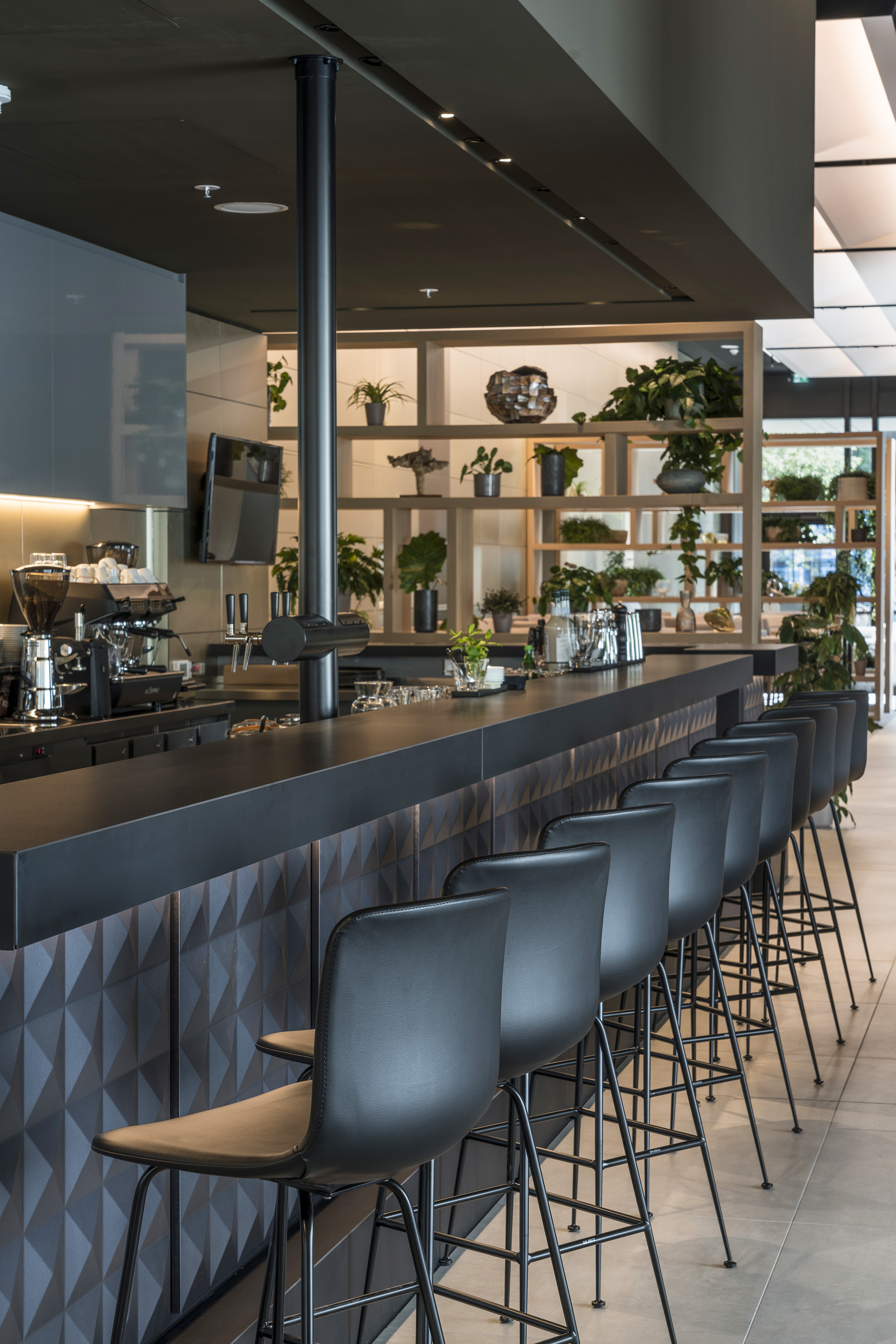 Modern cafe bar interior with black counter, bar stools, and green plants.