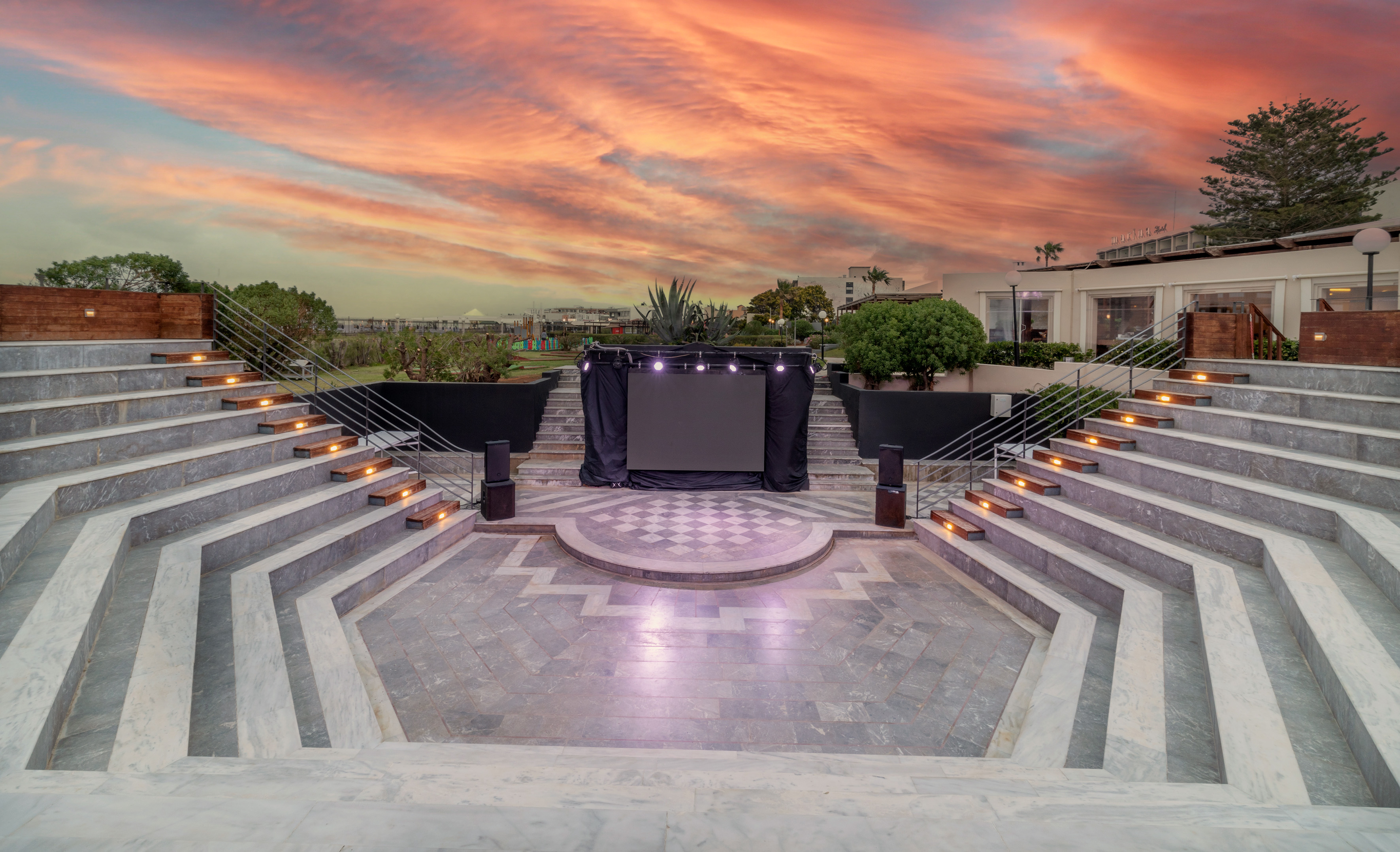 Resort outdoor amphitheater, tiered seating, LED stage, dramatic sunset.