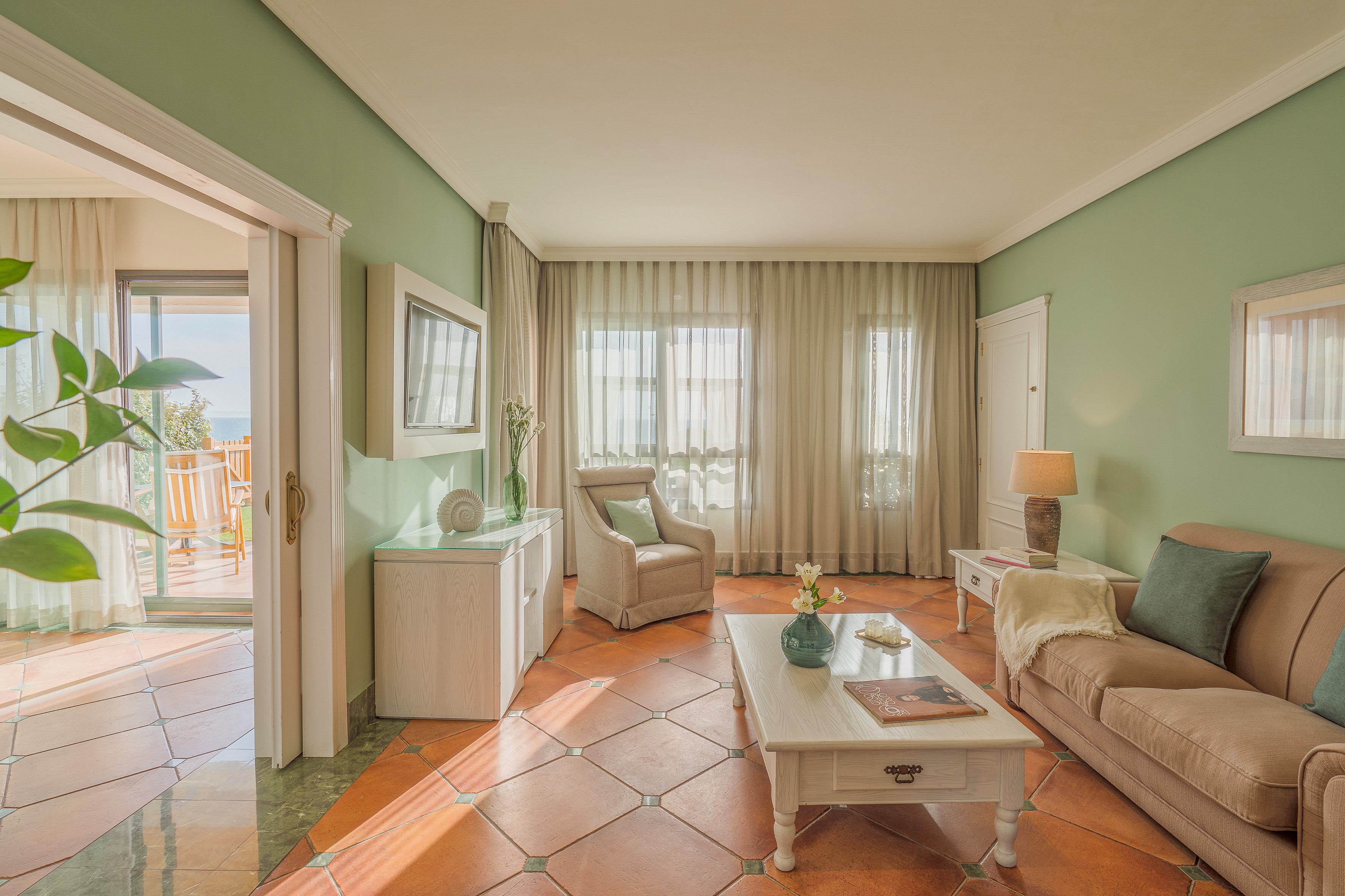 Mediterranean living room with green walls, terracotta floor, and sea view.