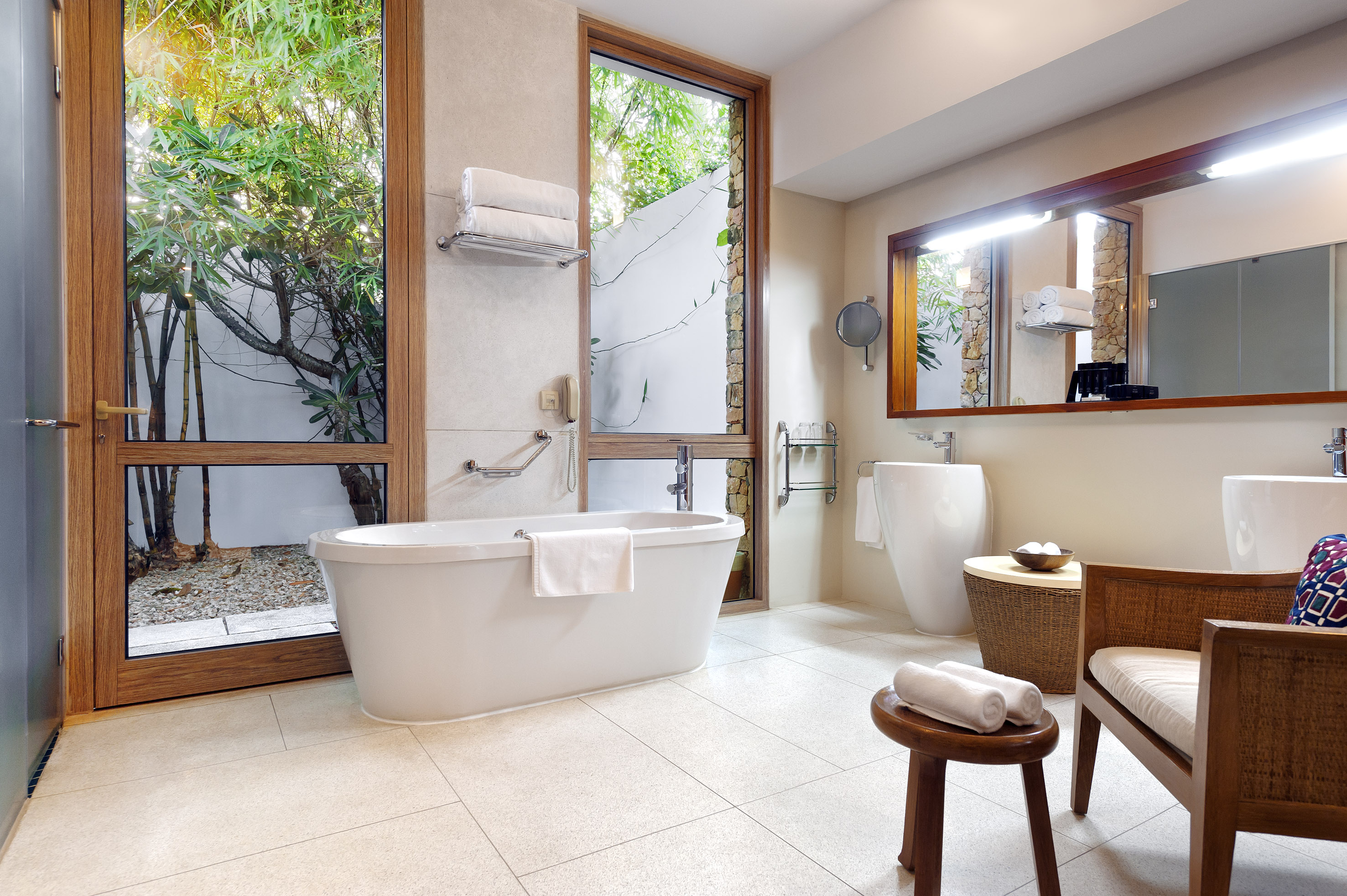 Modern bathroom with freestanding tub, double sinks, and lush garden view.