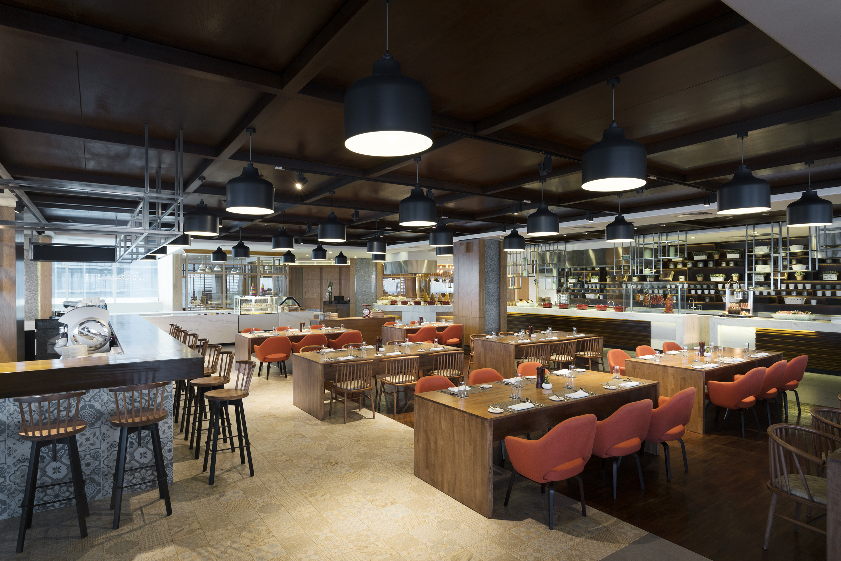 Modern restaurant dining room with wooden tables, orange chairs, buffet, and bar.