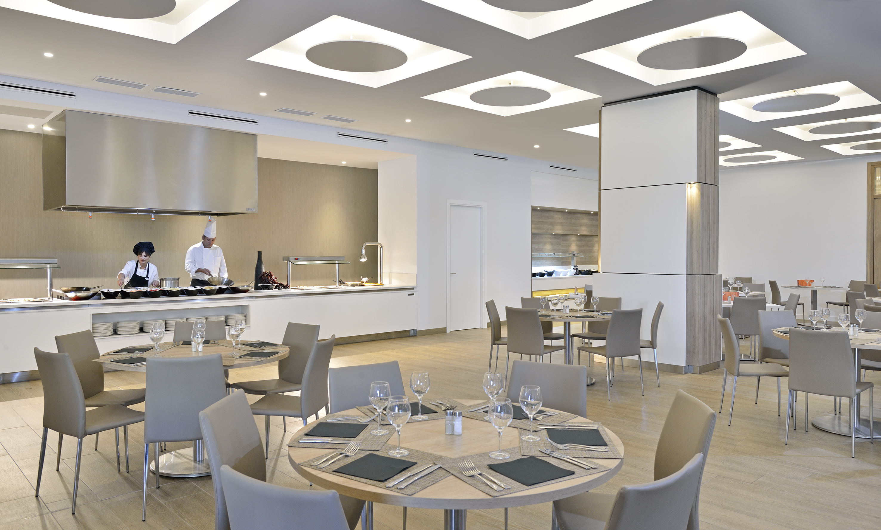 Modern restaurant buffet with chefs at live cooking station and dining tables.