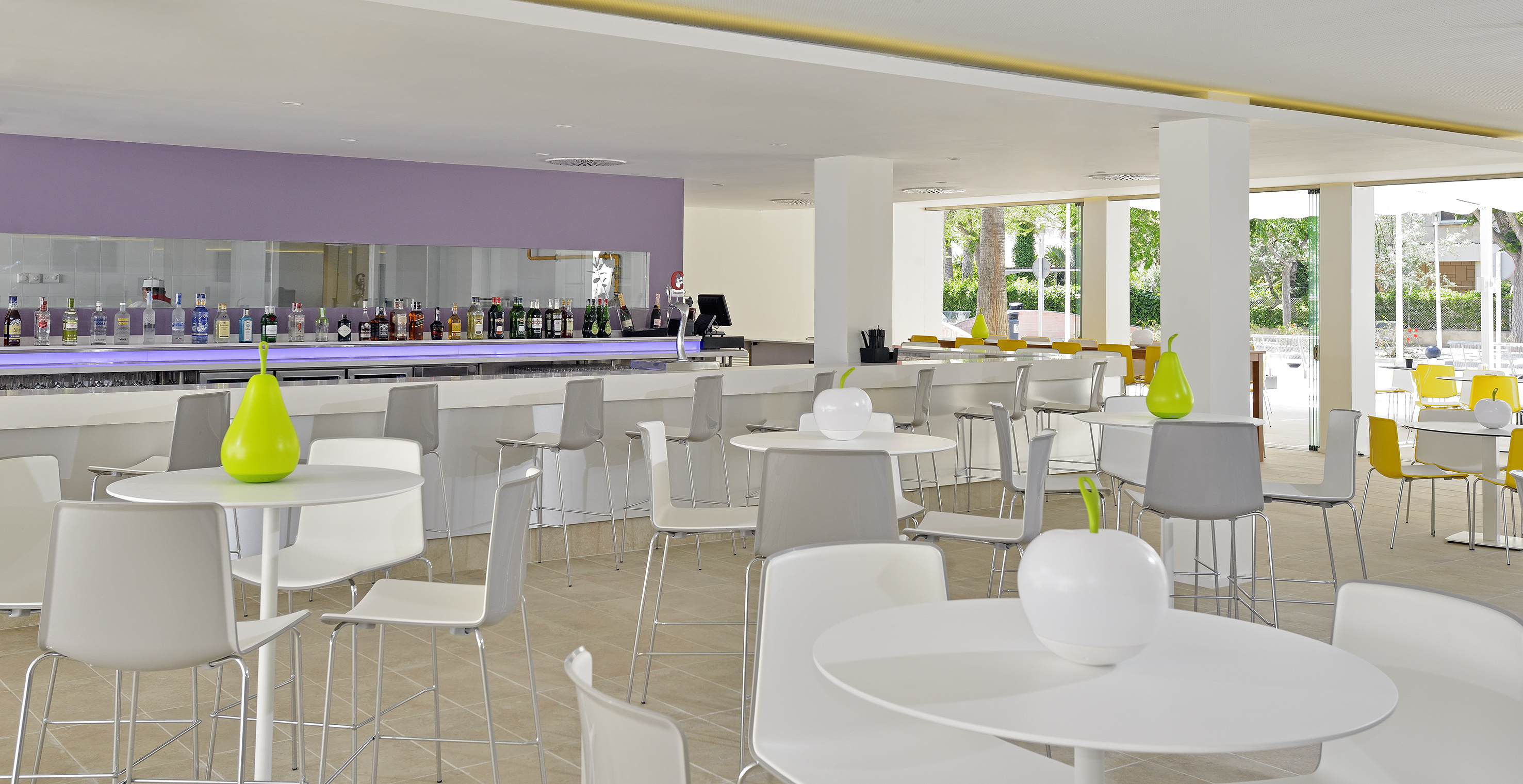 Modern hotel bar lounge, white seating, liquor display, bright garden view.