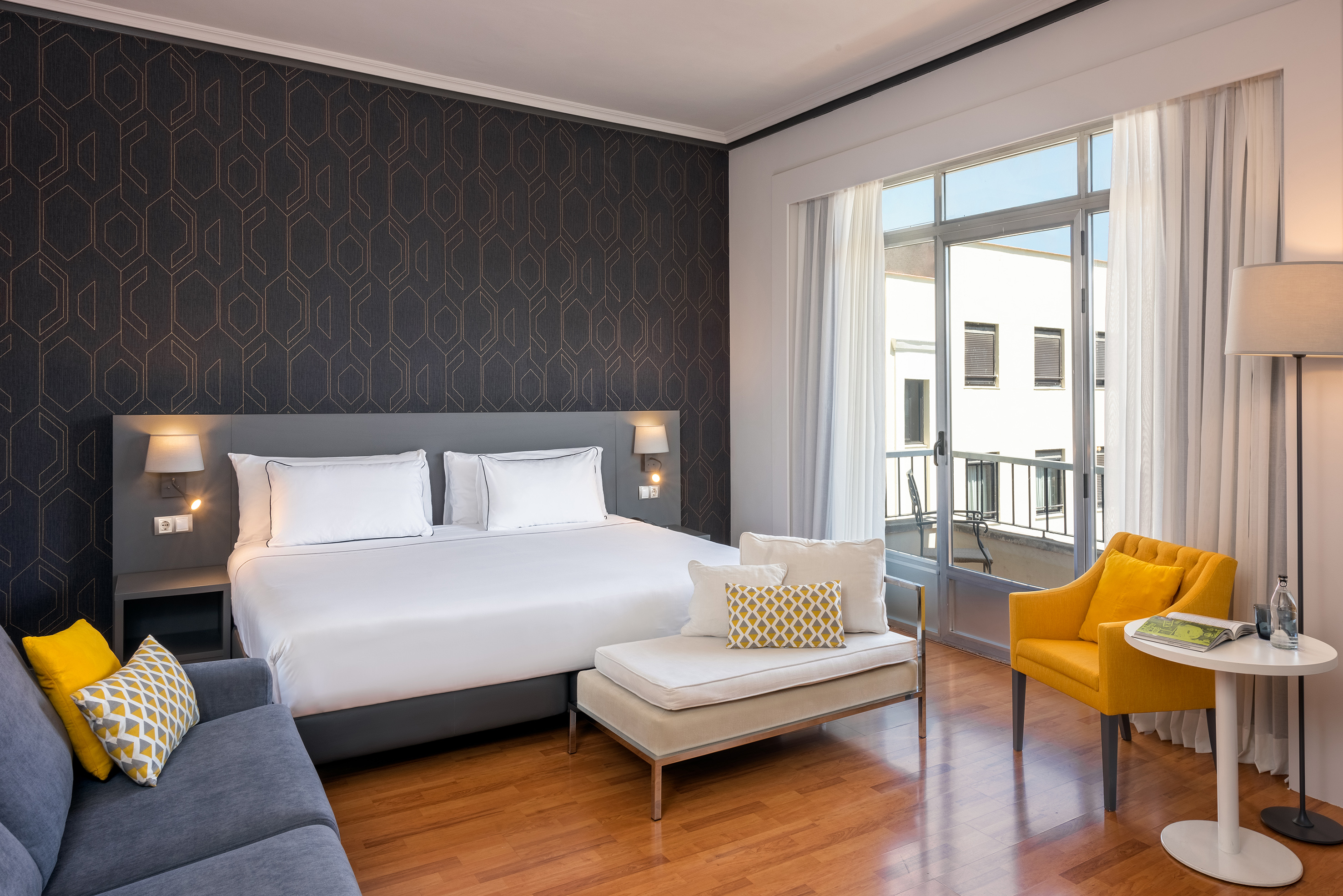 Modern hotel room with king bed, yellow decor, geometric wall, and balcony.