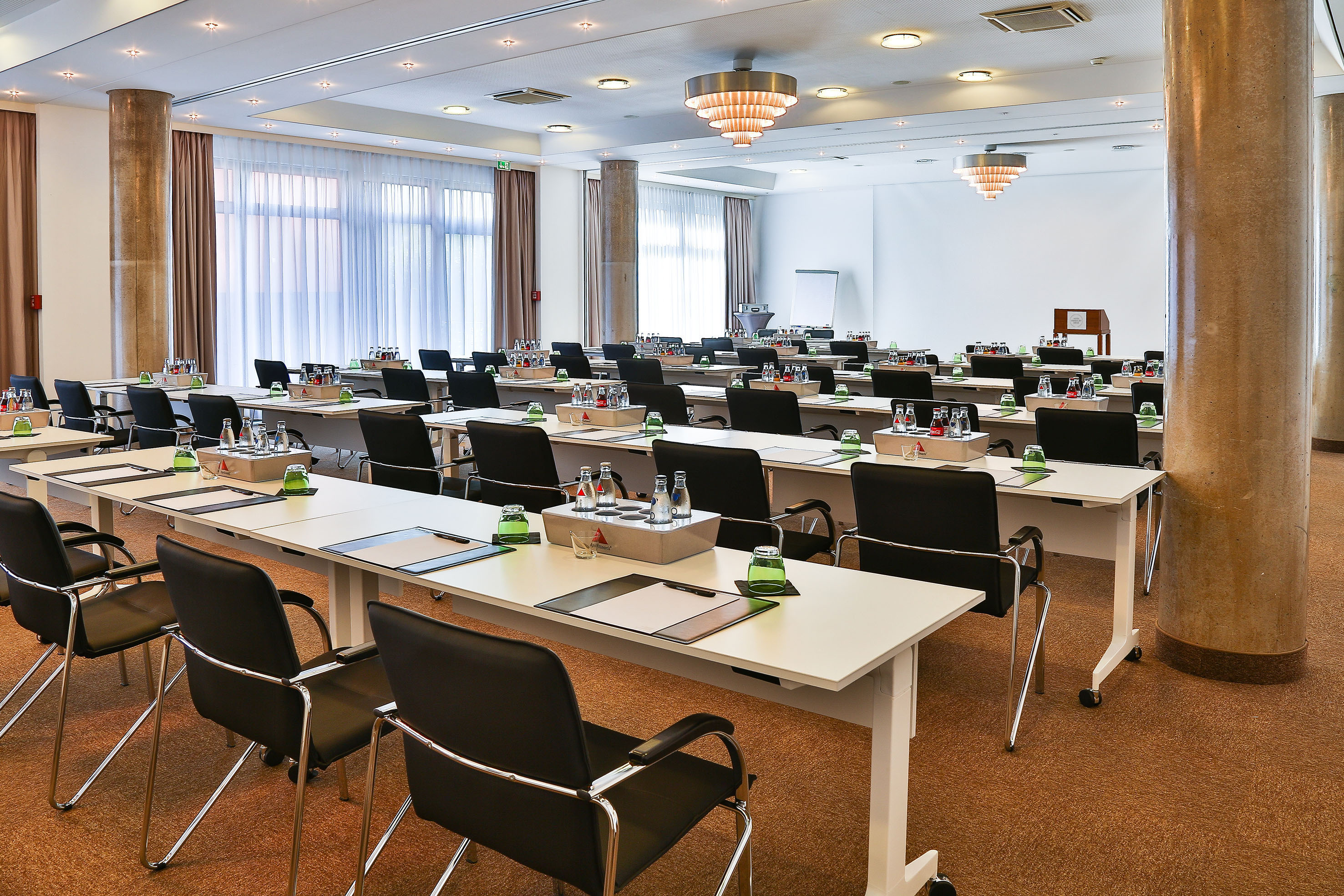 Conference room with tables, chairs, water bottles, and bright windows.
