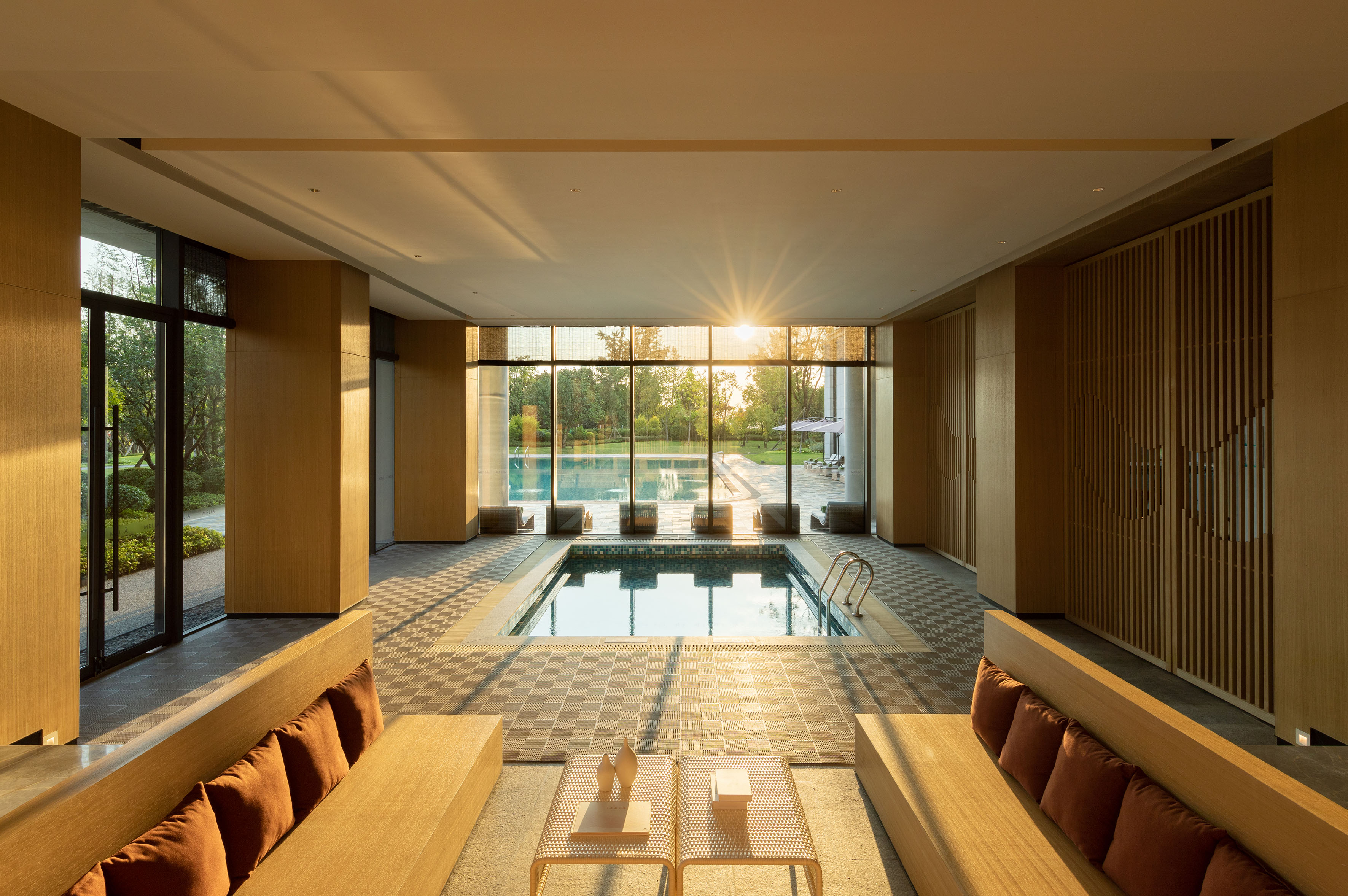 Indoor pool lounge with panoramic sunset view and outdoor swimming pool.