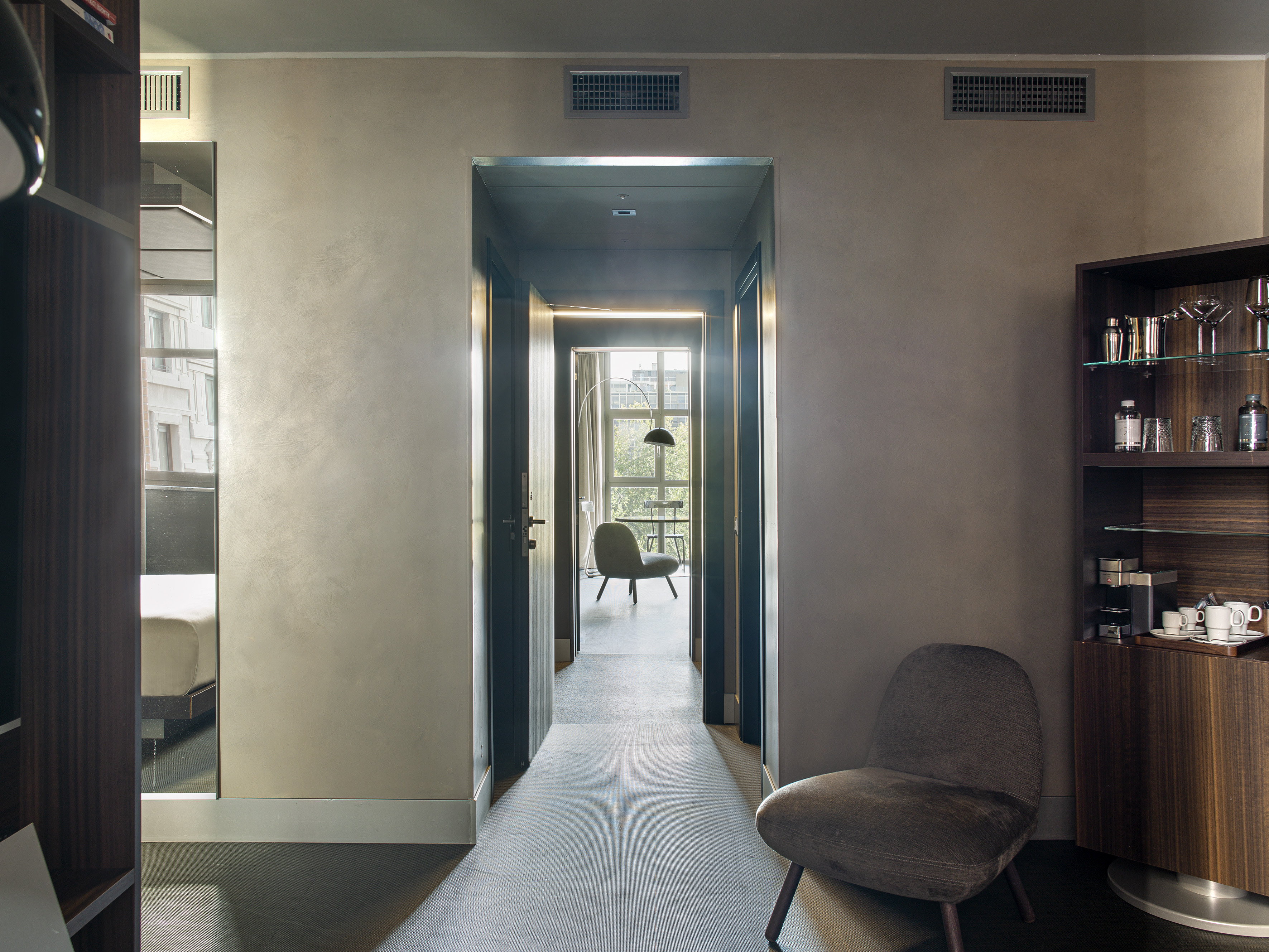Contemporary hotel room entryway with minibar, accent chair, and hallway.