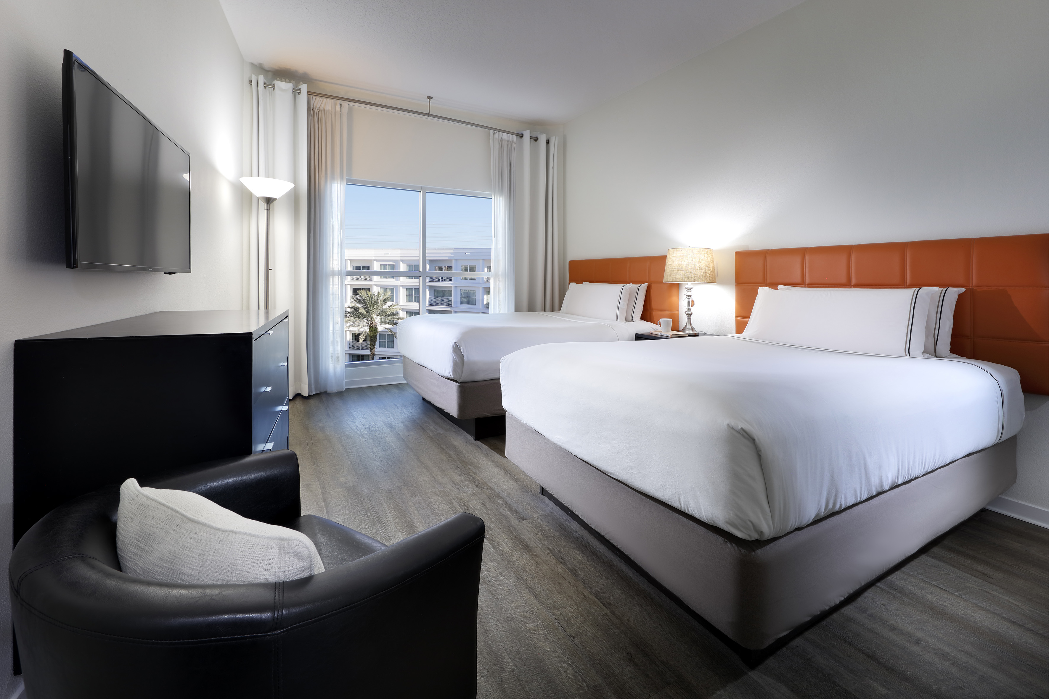 Hotel room with two queen beds, orange headboards, flat-screen TV, and window.