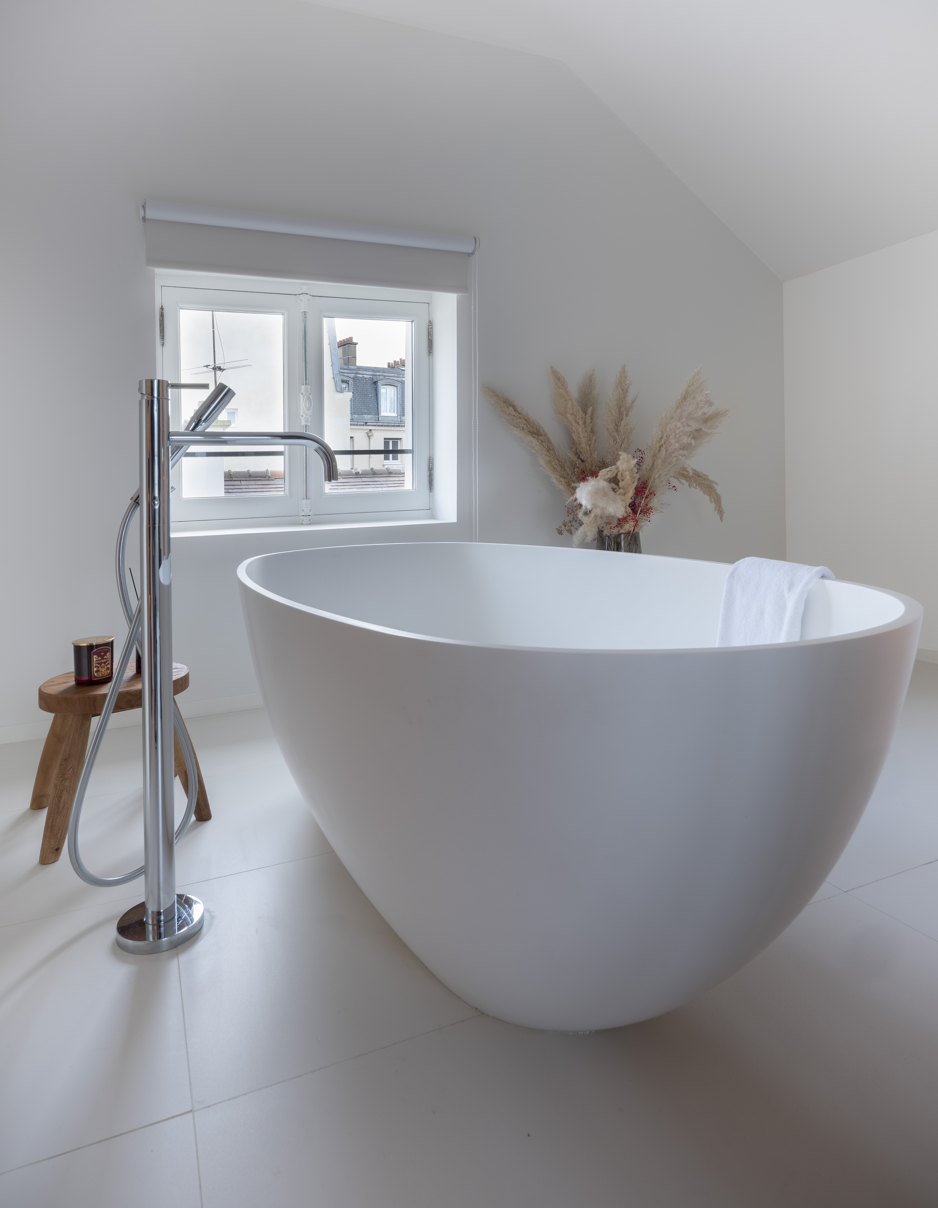 Modern bathroom with white freestanding bathtub, chrome faucet, and window.