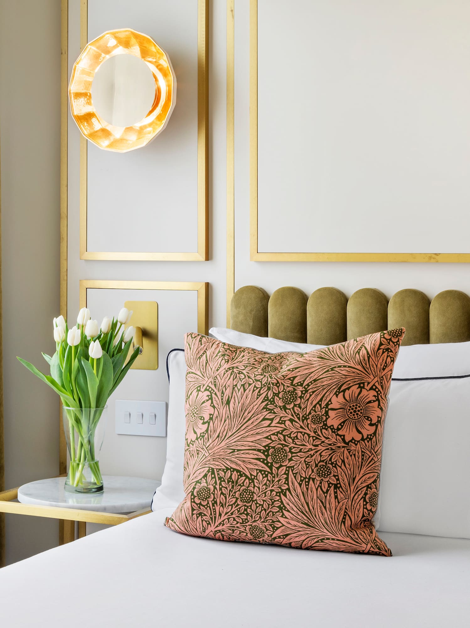Bedroom with floral pillows, green headboard, white tulips, and gold wall accents.