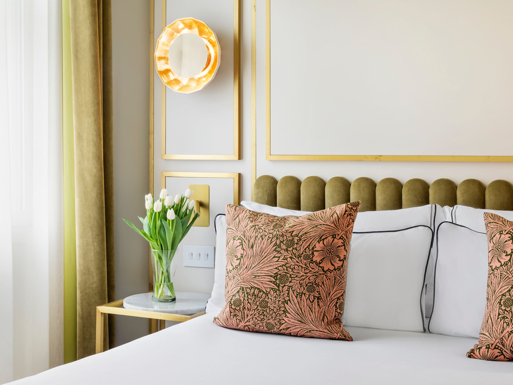Bedroom with floral pillows, green headboard, white tulips, and gold wall accents.
