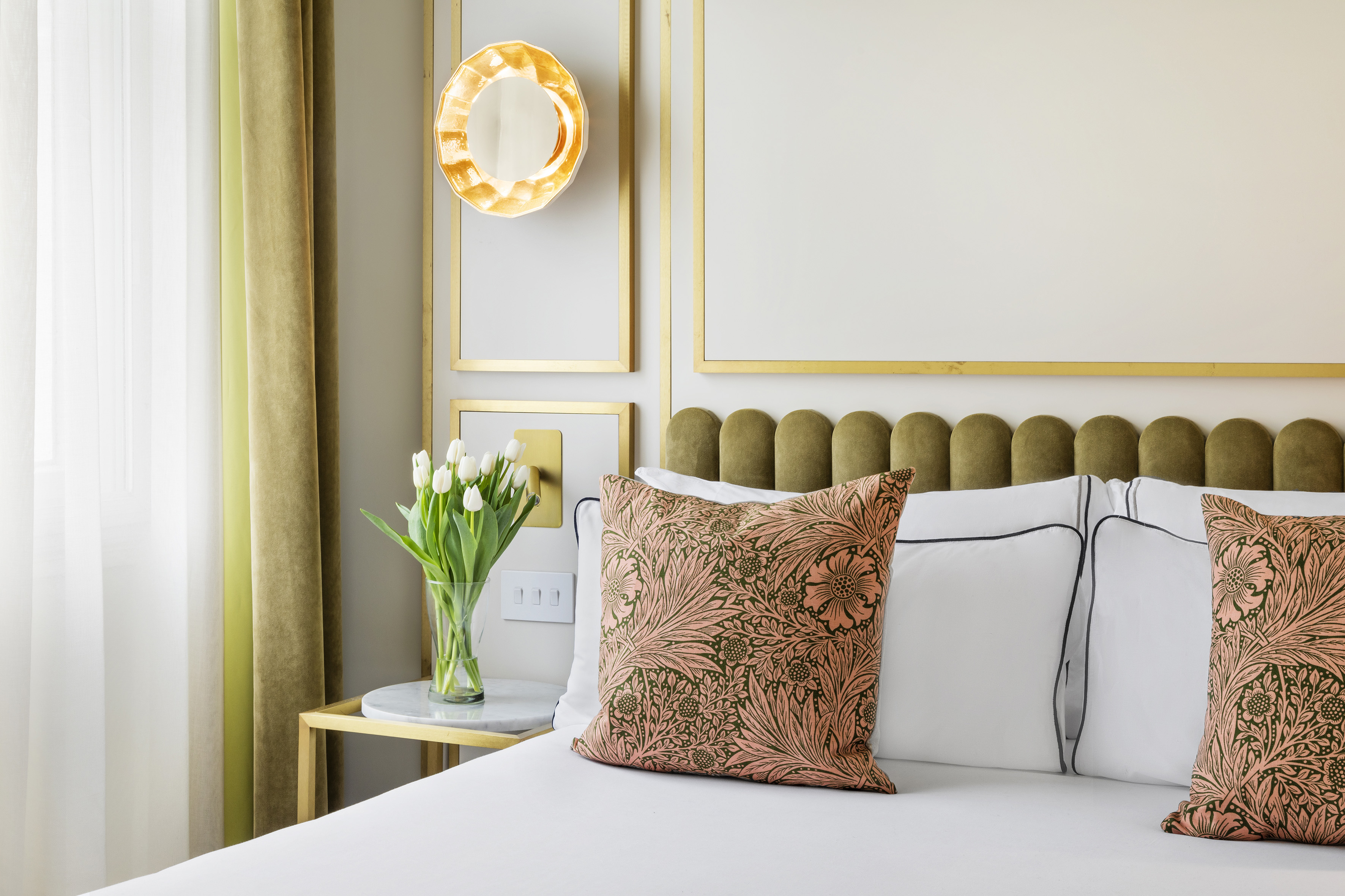 Luxury bedroom with green velvet headboard, floral pillows, and white tulips.