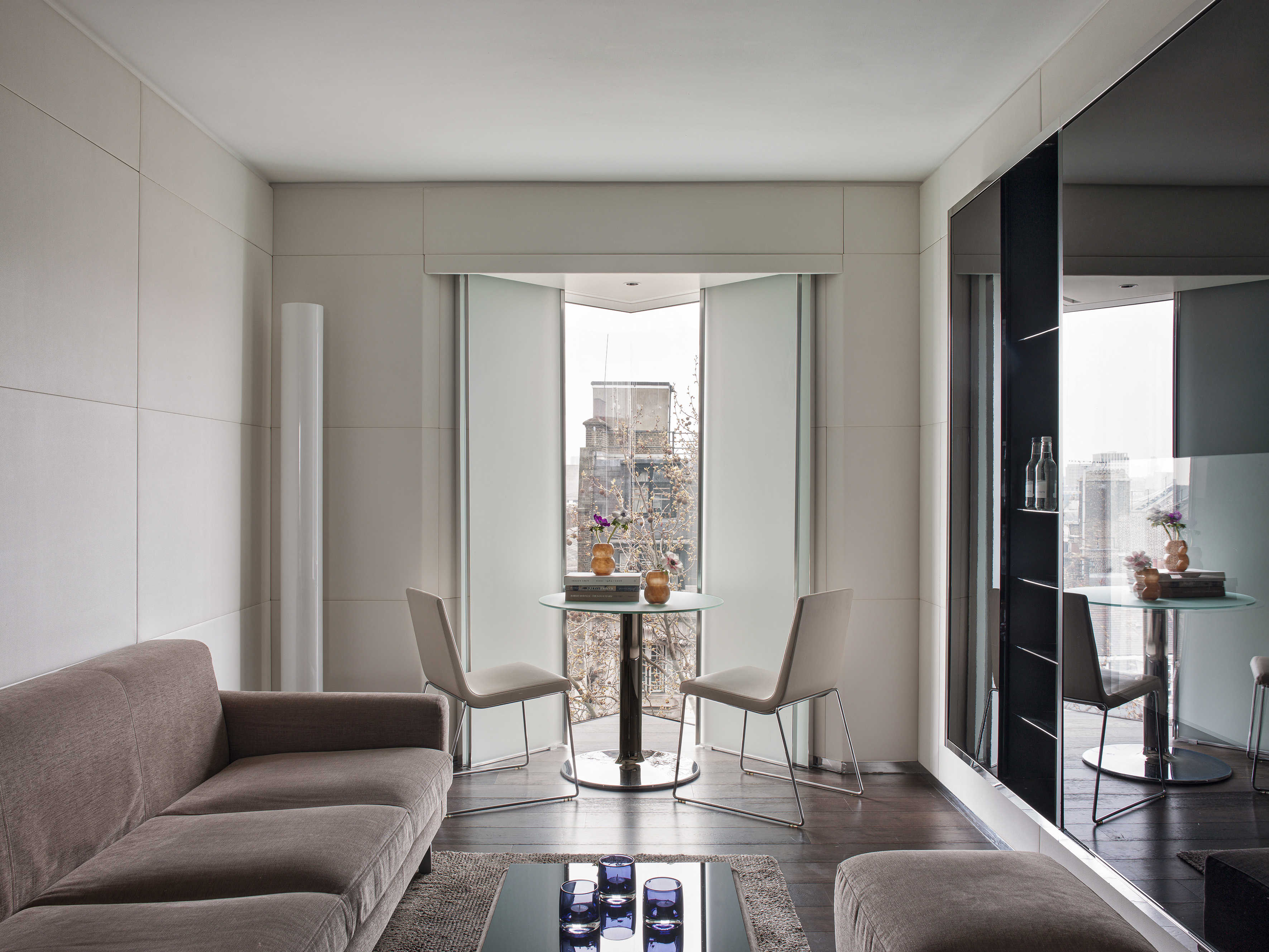 Contemporary living room with taupe sofa, glass table, and city view window.