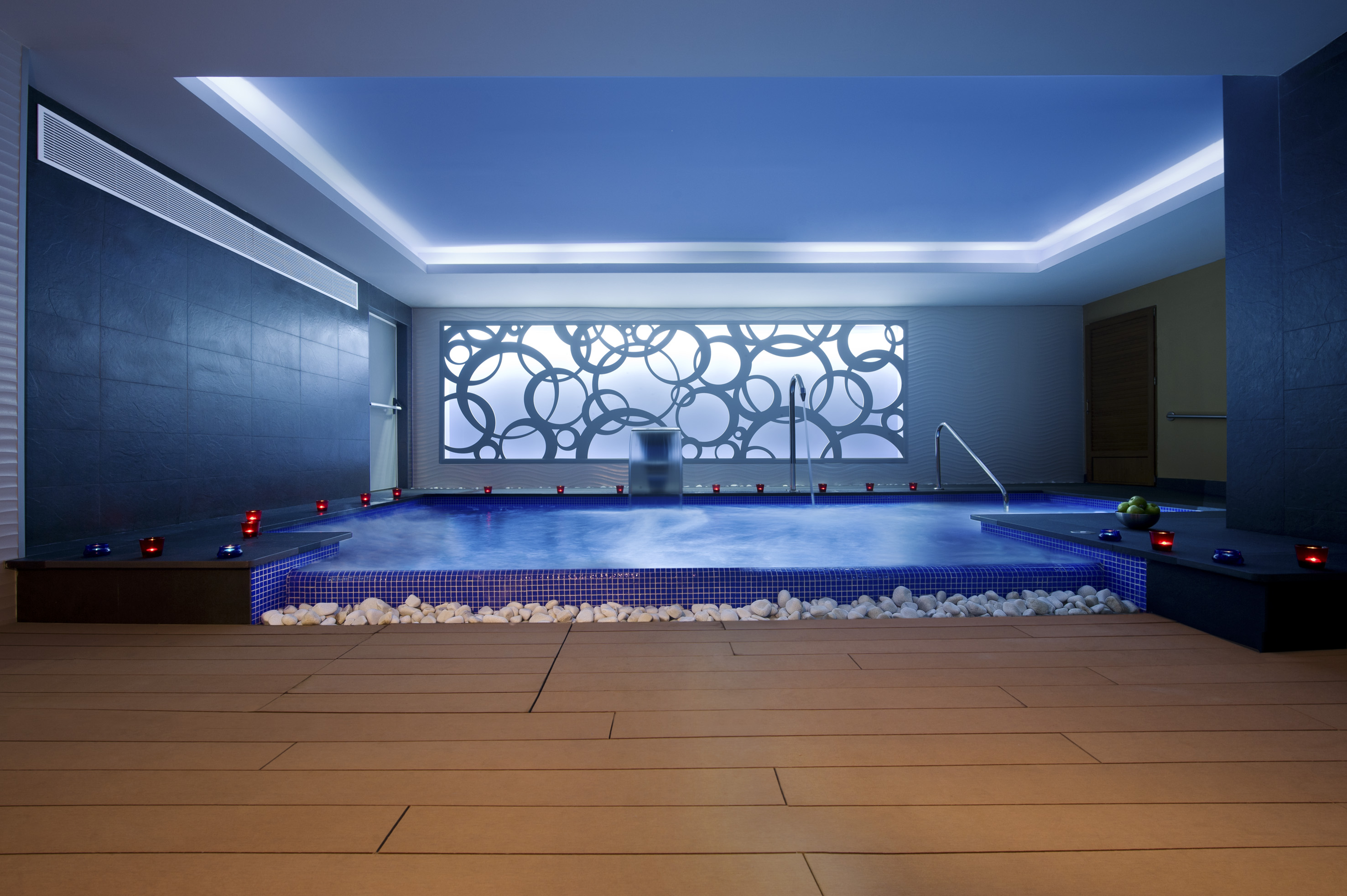 Luxury indoor spa pool with blue lighting, mosaic tiles, and modern decor.