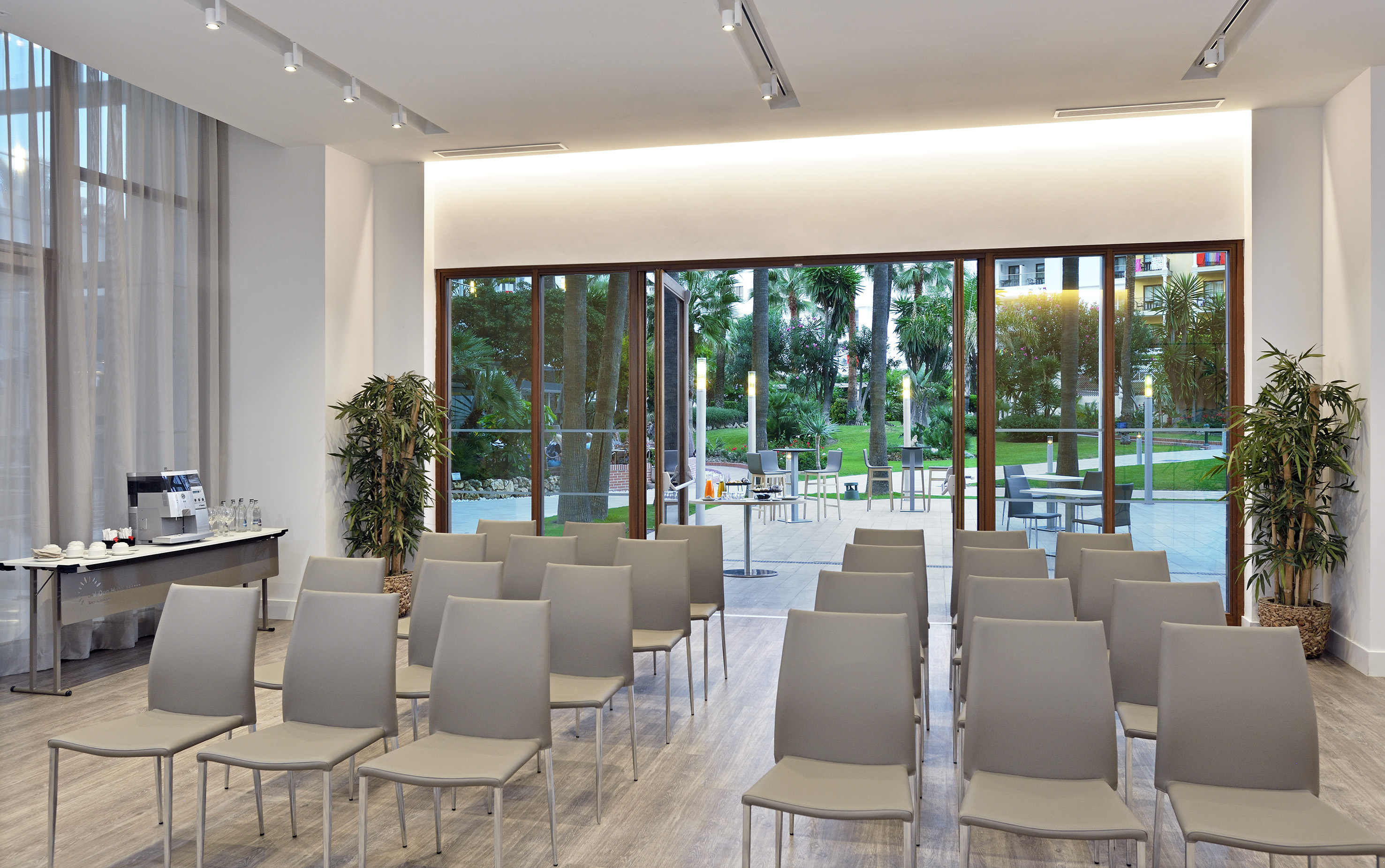 Bright conference room with chairs, coffee station, and lush tropical garden view.
