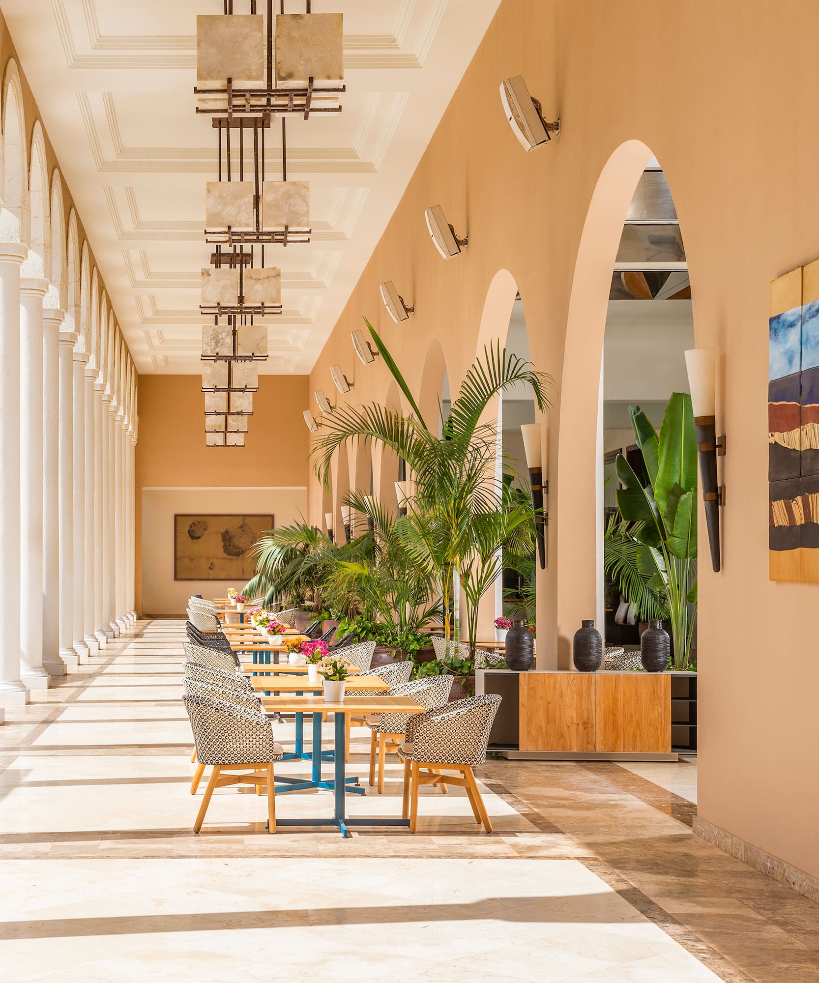 a long hallway with white columns and tables and chairs