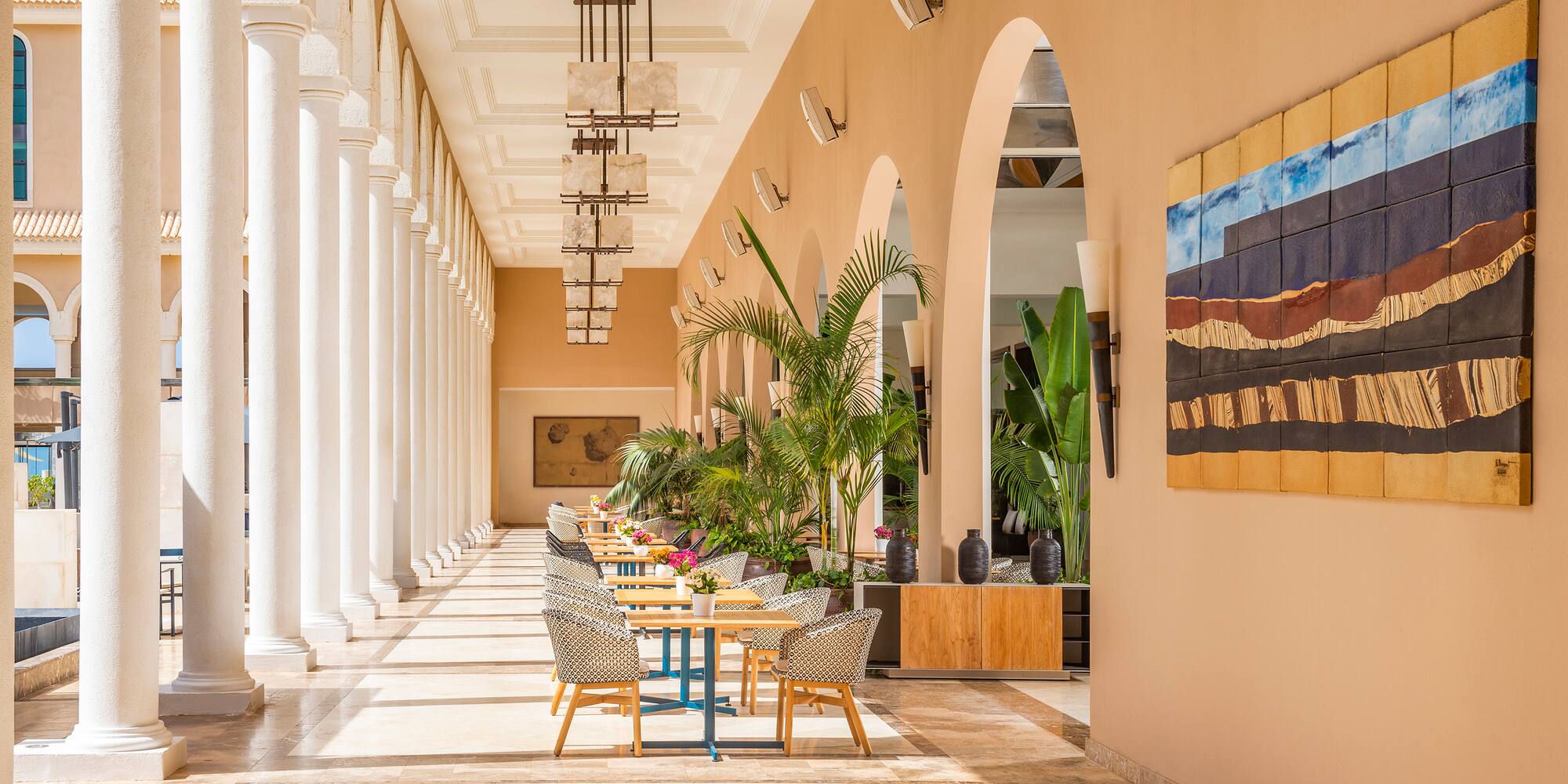 a long hallway with white columns and tables and chairs