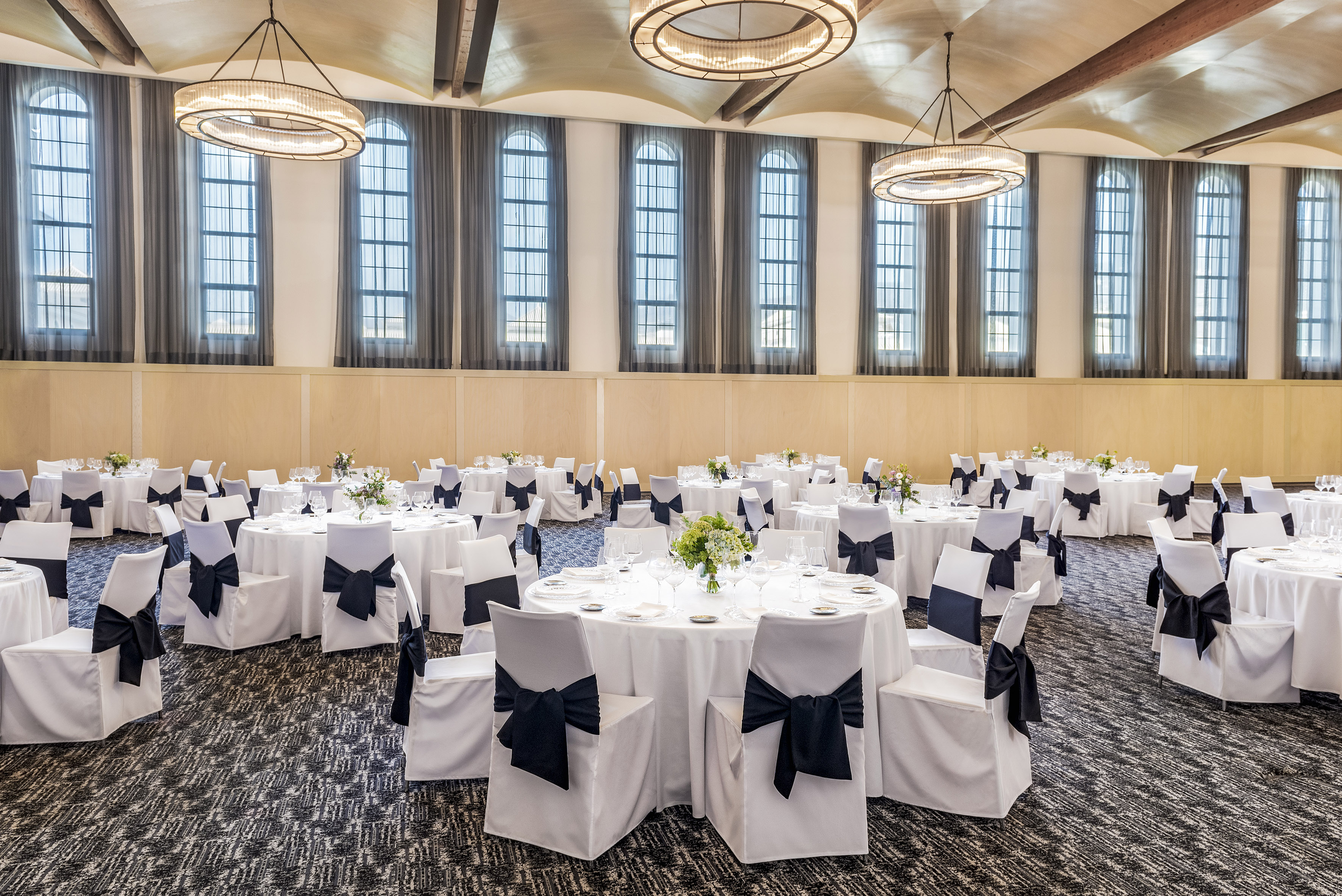 Elegant ballroom with set round tables, white linens, black bows, chandeliers.