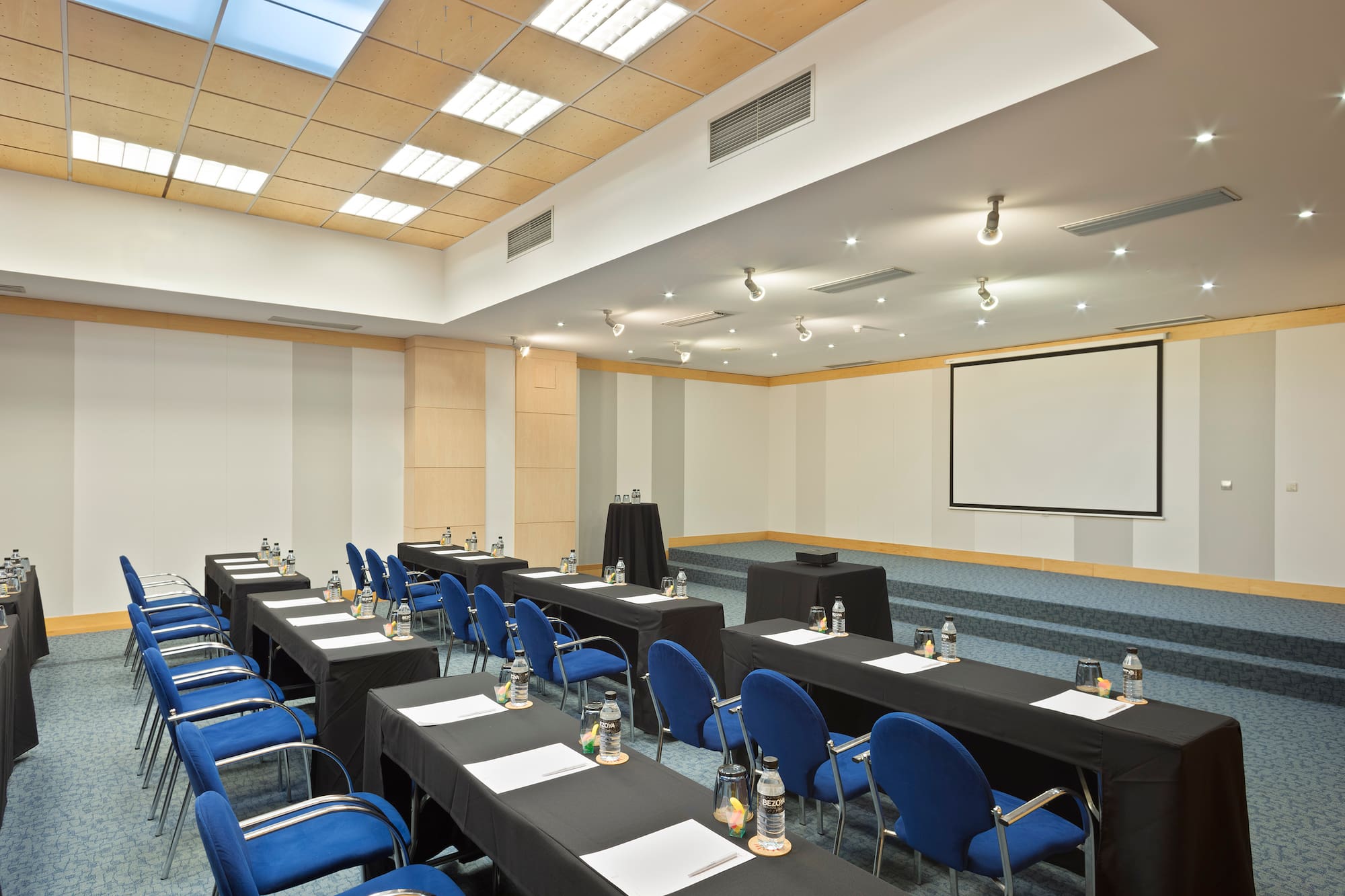 Meeting room setup: blue chairs, black tables, projector screen.