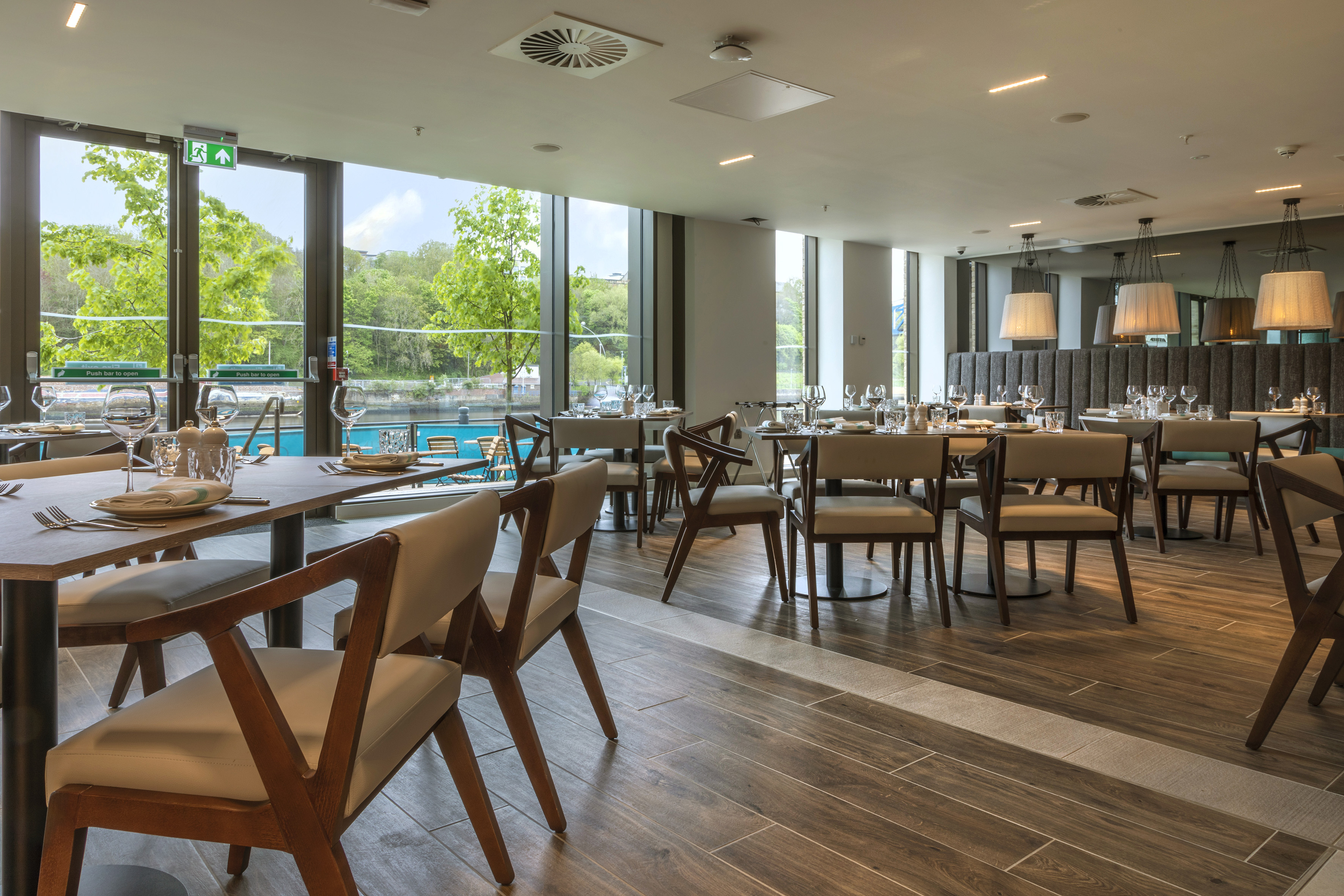 Modern restaurant interior, set tables, stylish chairs, and a scenic water view.
