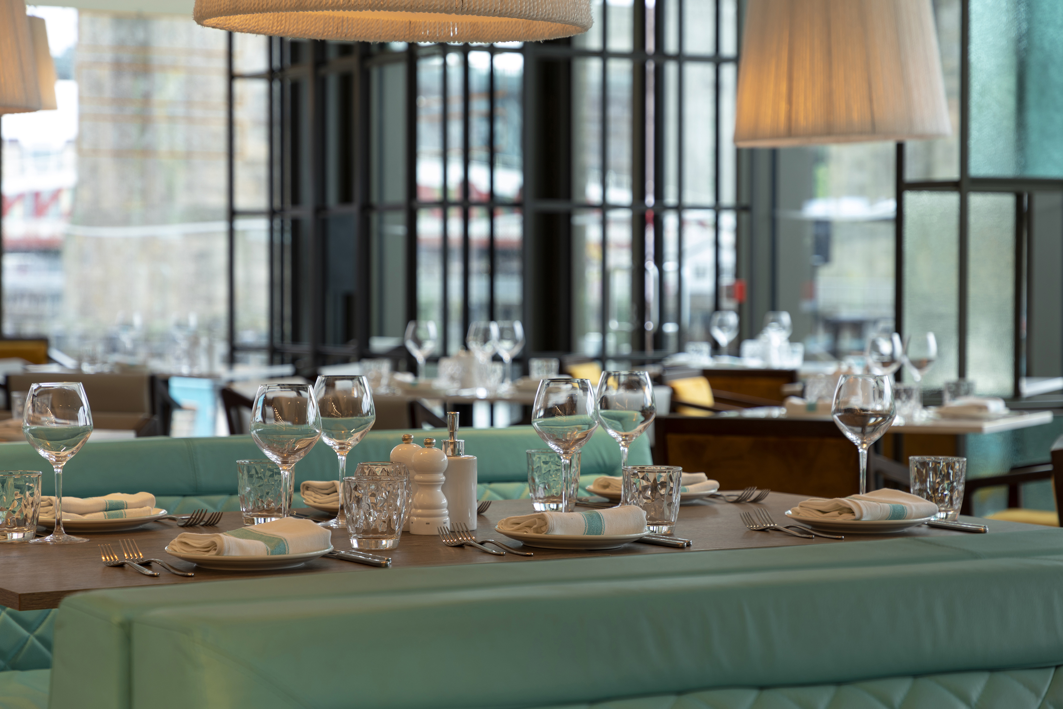 Restaurant dining table with teal booth seating, set for guests, modern interior.