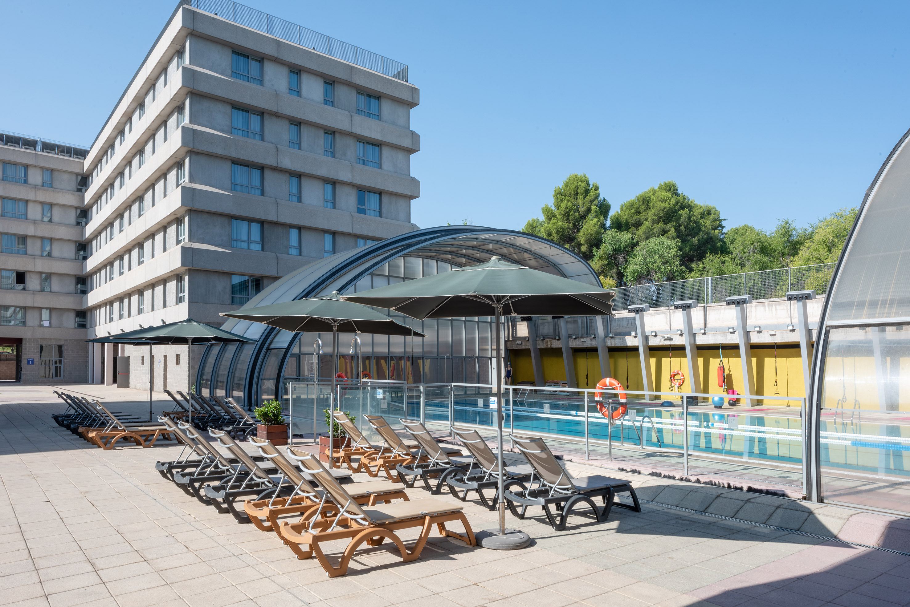 Hotel swimming pool area with sunbeds, umbrellas, and covered pool section.