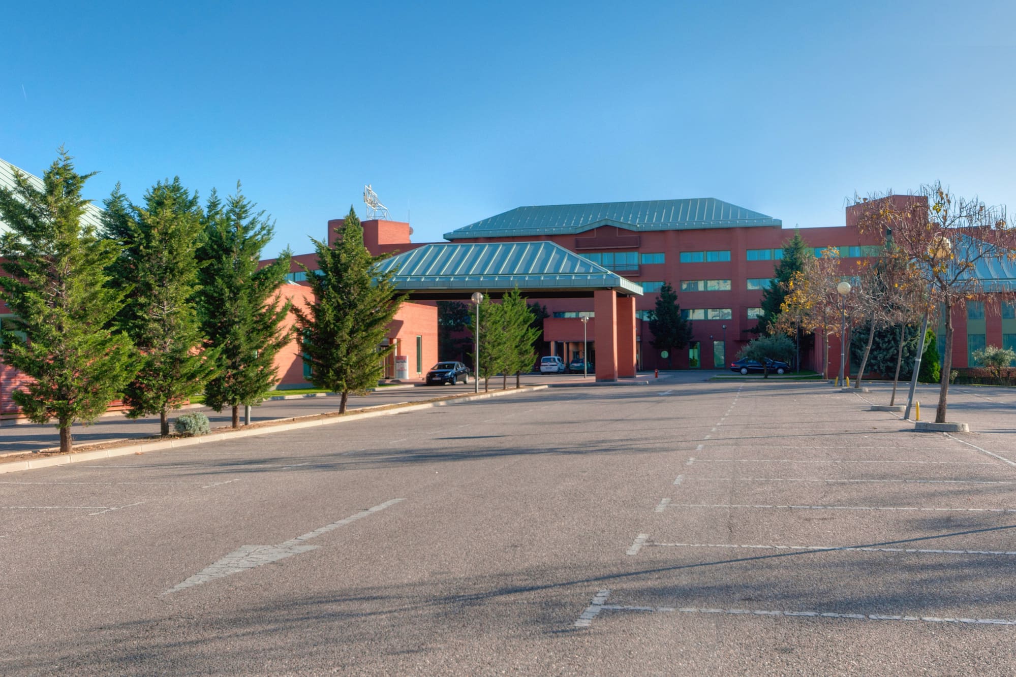 Red brick building, covered entry, empty parking lot, and green trees.
